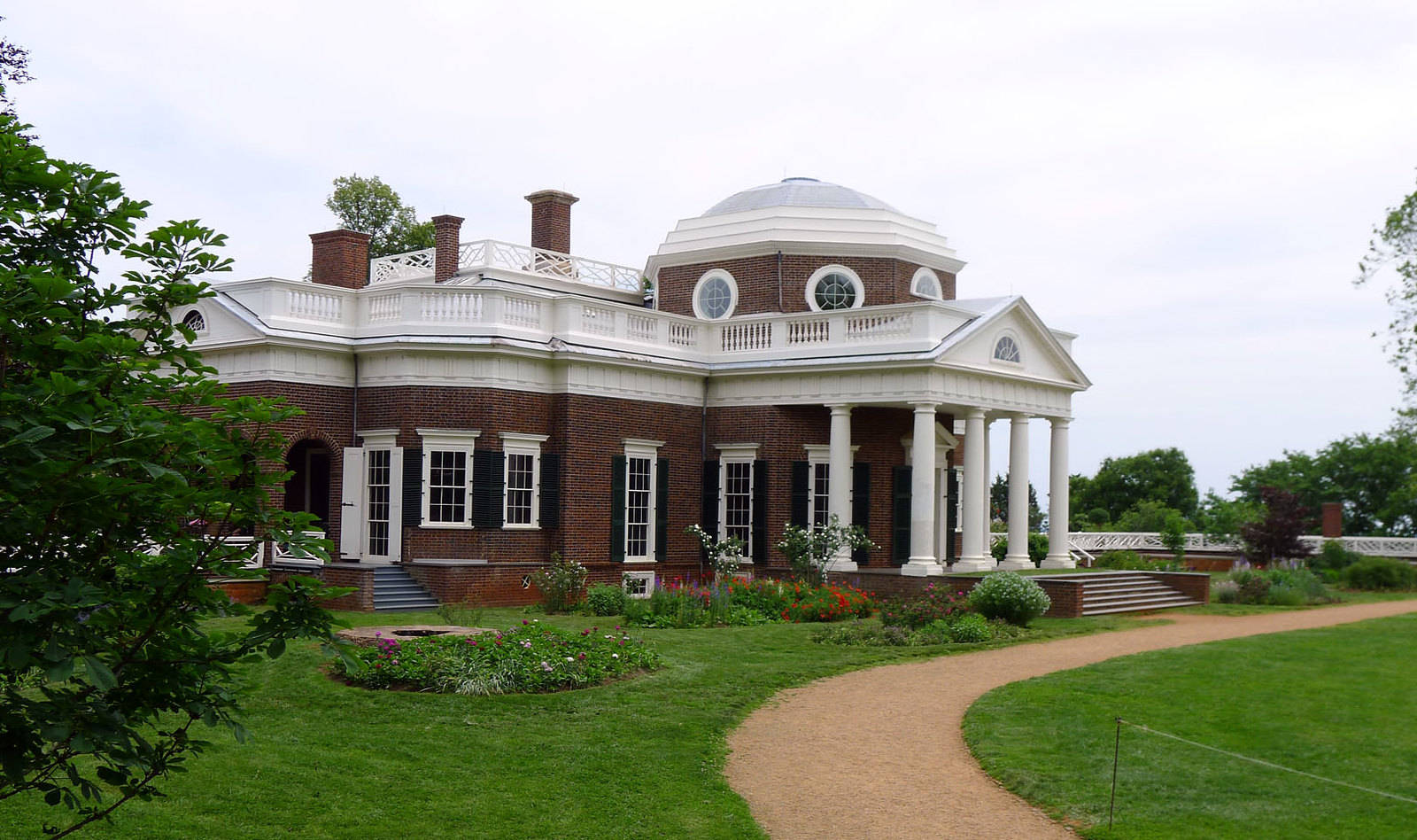 Virginia 桌布 壁紙 — 一座宏偉的新古典主義磚砌豪宅，擁有白色柱子和圓頂，矗立在鬱鬱蔥蔥的綠色草坪和蜿蜒小徑之中，天空多雲。