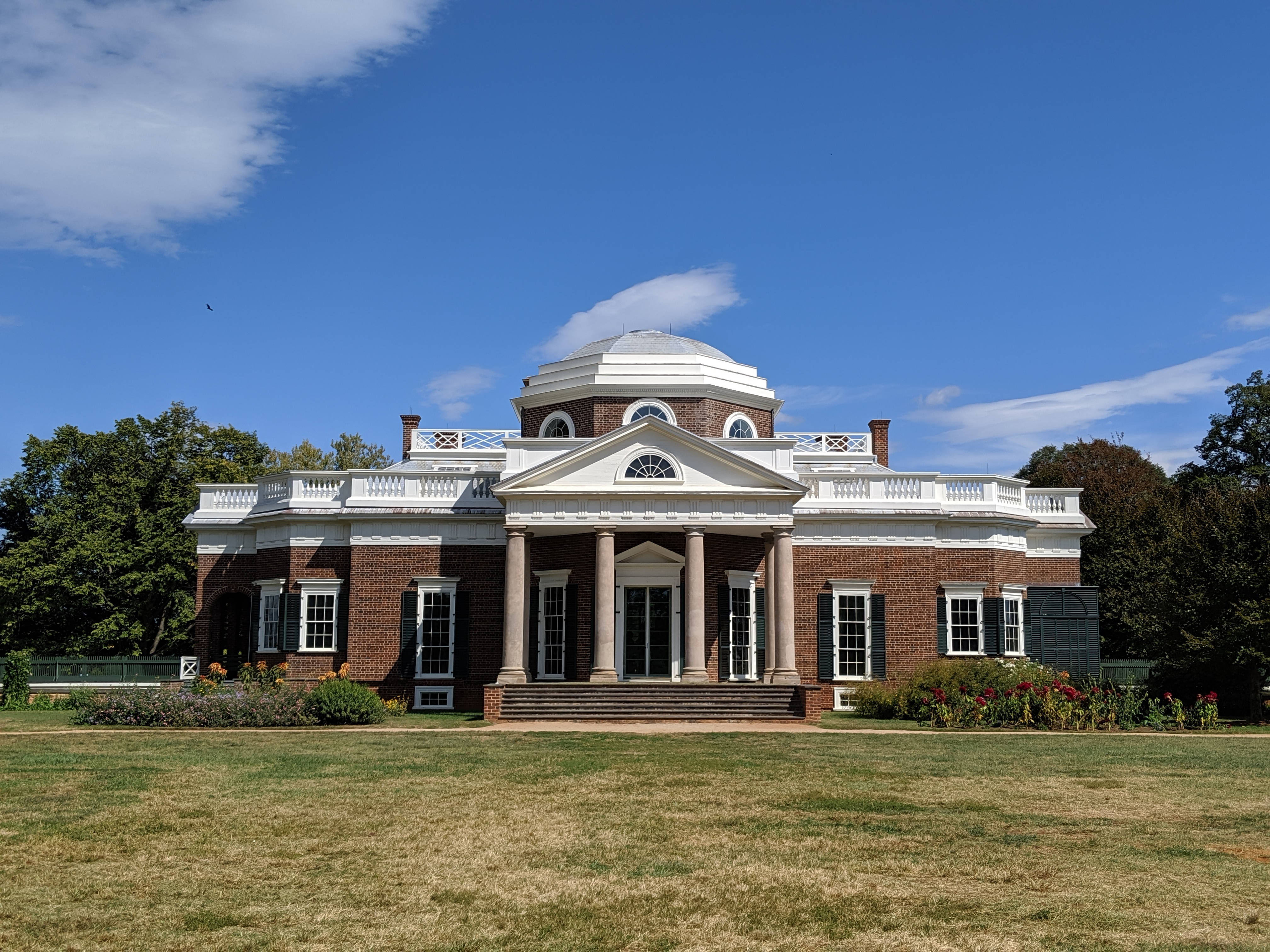 Virginia 桌布 壁紙 — 一座宏偉的新古典主義磚砌豪宅，擁有白色柱子和圓頂，矗立在晴朗的藍天下，天空中有稀疏的雲朵。