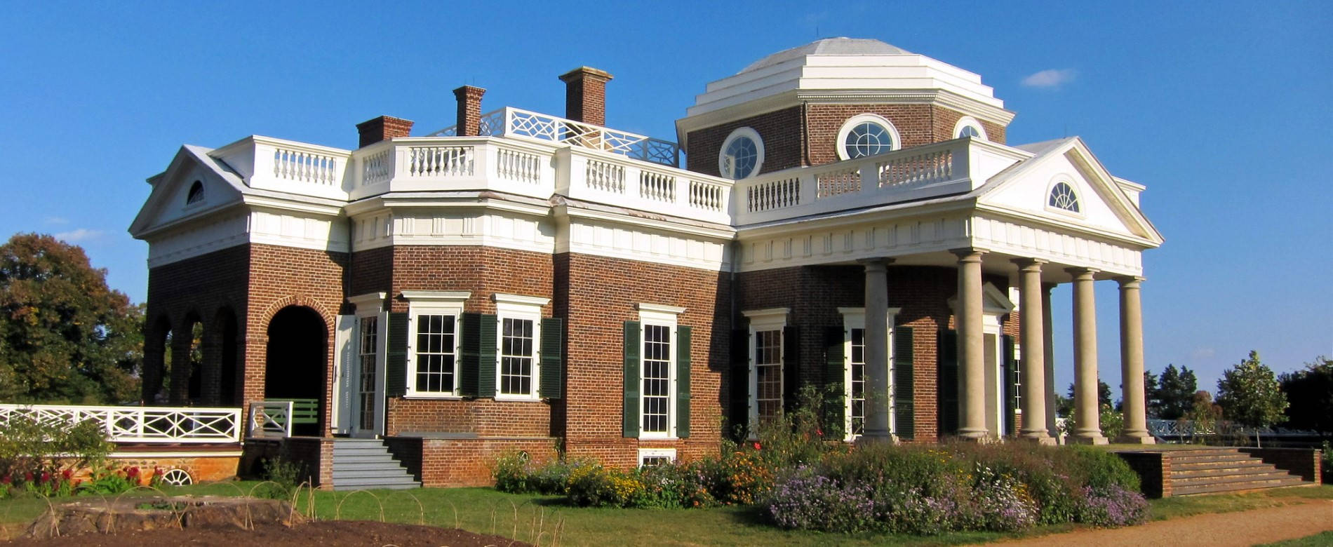 Virginia 桌布 壁紙 — 一座宏偉的新古典主義磚砌豪宅，擁有白色柱子和圓頂，矗立在晴朗的藍天下，周圍是修剪整齊的花園。