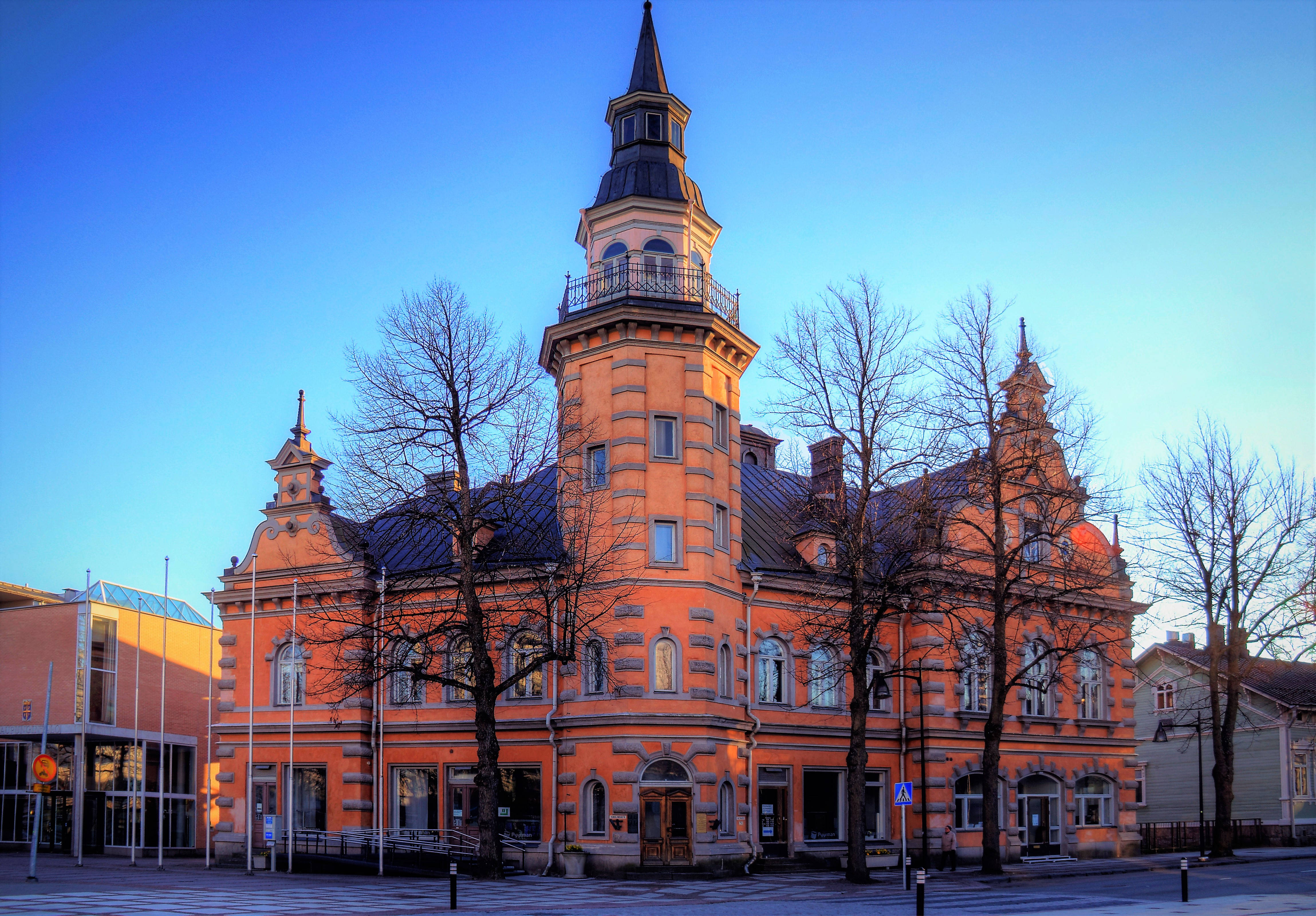 Finland 桌布 壁紙 — 一座宏偉的橙色歷史建築，擁有高聳的尖塔，矗立在清澈的藍天下，光禿的樹木在黃金時刻勾勒出它的外牆。