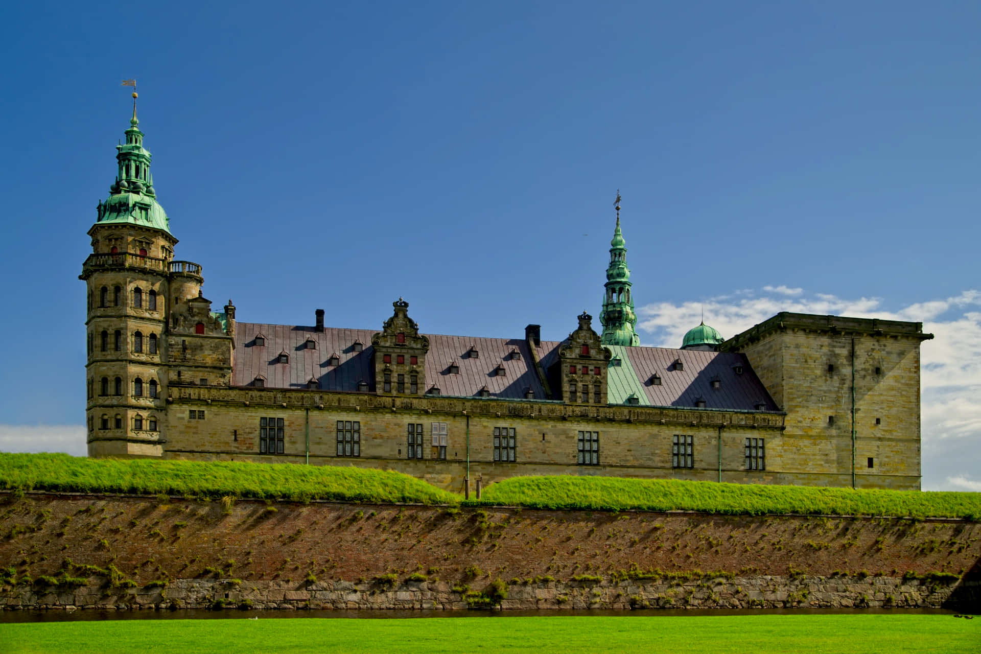Denmark 桌布 壁紙 — 一座宏偉的歷史城堡，擁有綠色銅屋頂和石塔，在晴朗的藍天下，矗立在充滿活力的綠色草坪上。