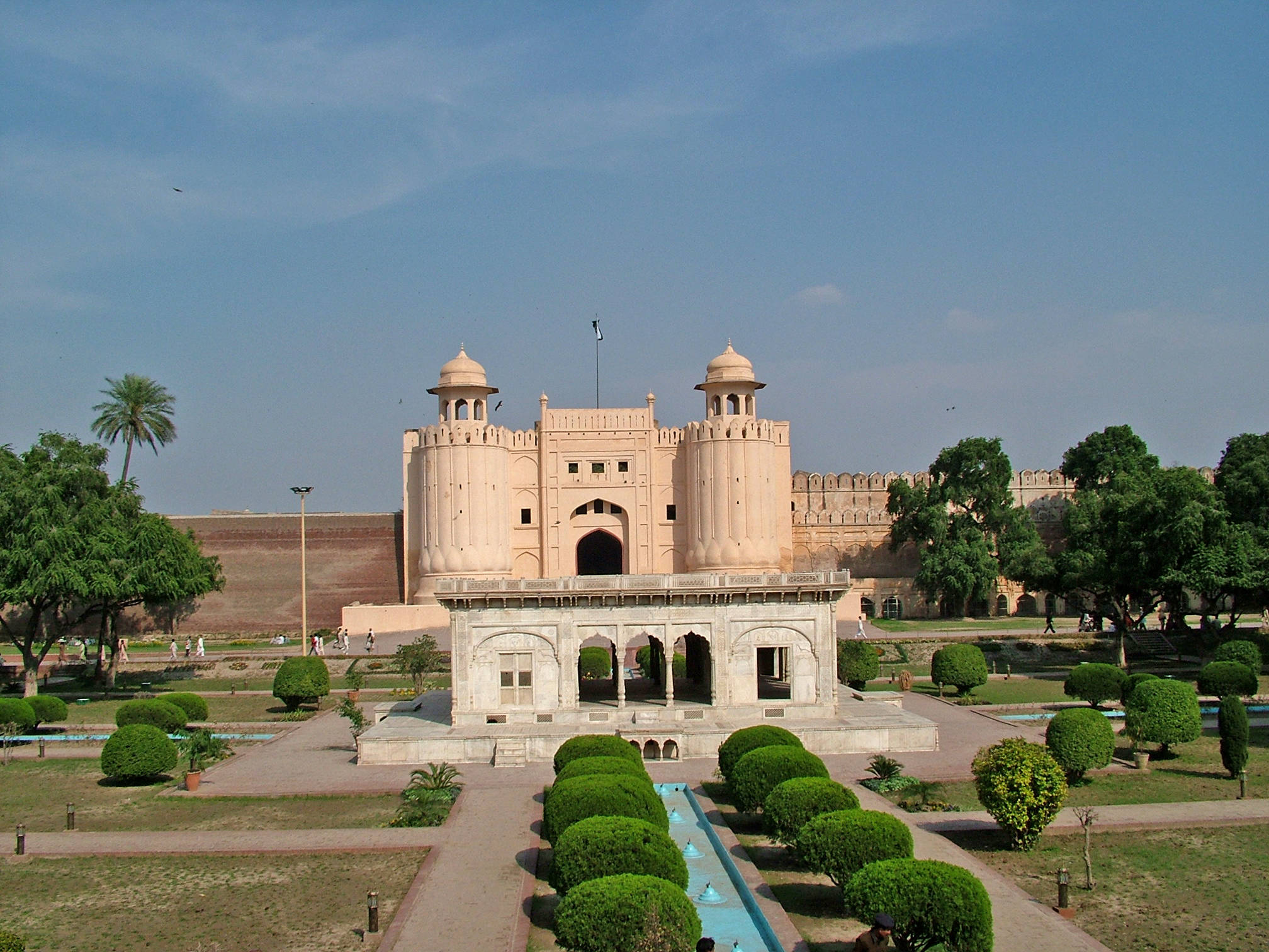 Lahore 桌布 壁紙 — 一座宏偉的歷史堡壘，擁有粉紅色砂岩塔樓和拱形大門，周圍是修剪整齊的花園，在晴朗的藍天下。