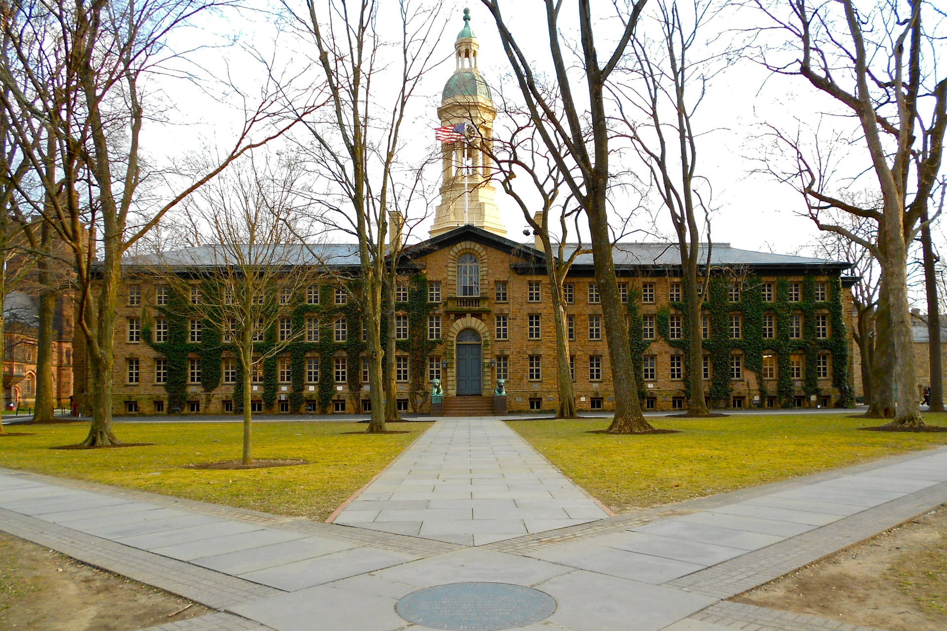  壁紙 — 一座宏偉的歷史大學建築，中央有一座鐘樓，周圍是光禿禿的冬季樹木和一條通往拱形入口的鋪砌步道。