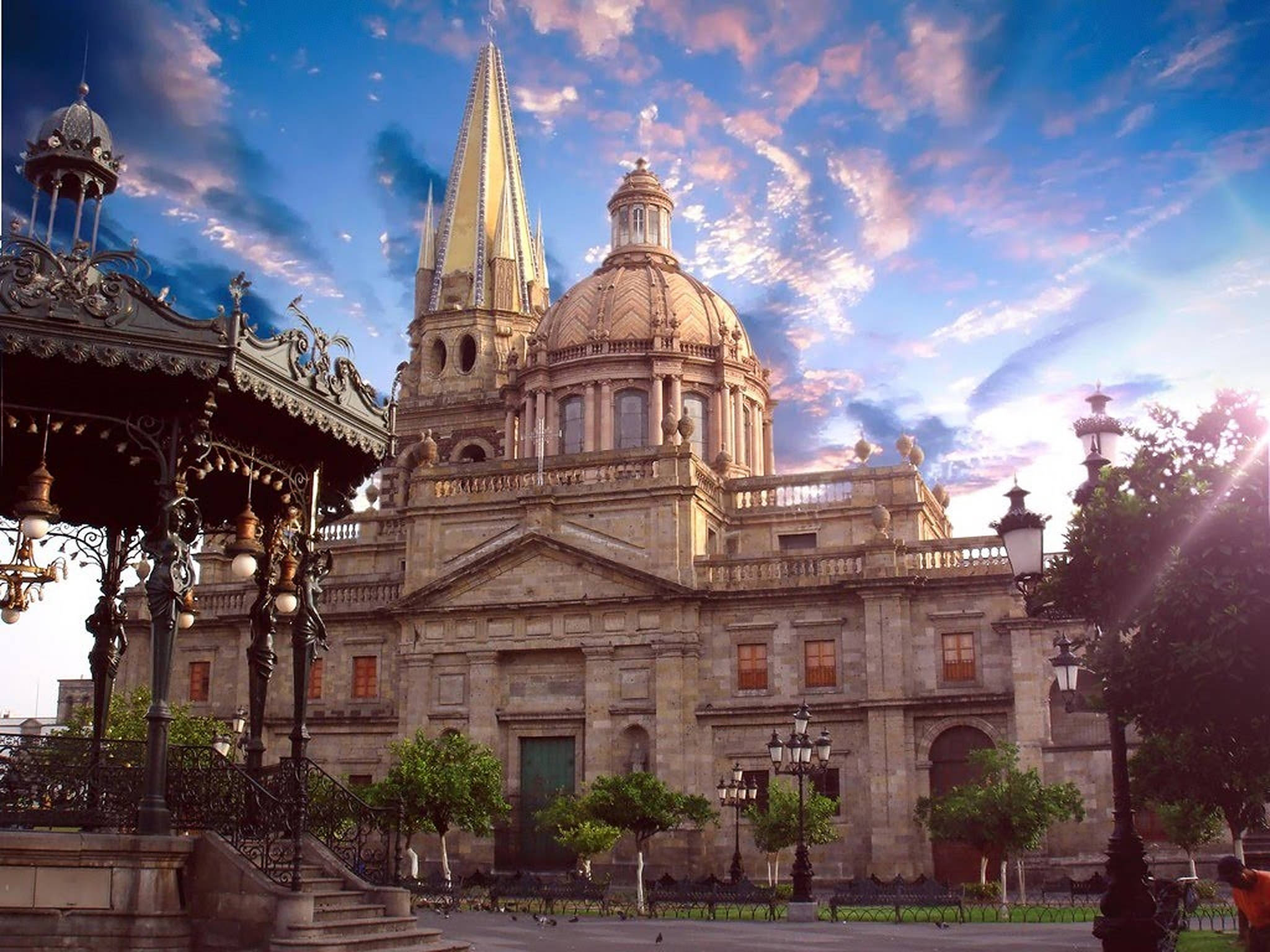 Guadalajara 桌布 壁紙 — 一座宏偉的歷史大教堂，擁有金色尖頂和圓頂，矗立在充滿活力的日落天空下，天空中有散落的雲彩。