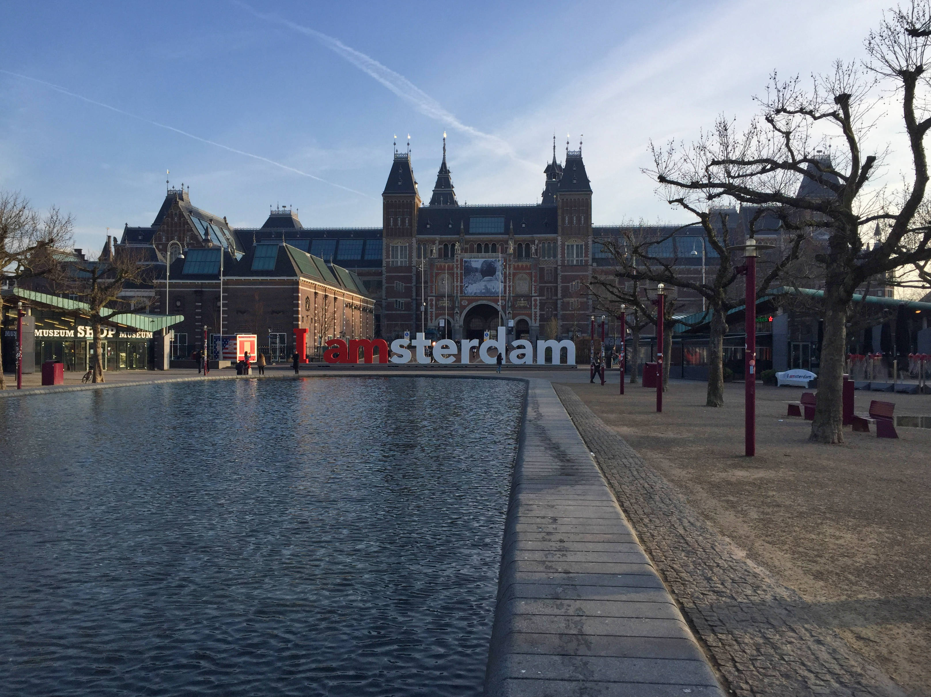 Museum 桌布 壁紙 — 一座宏偉的歷史建築，帶有尖塔，矗立在反射池和「I amsterdam」標誌後面，在清澈的藍天下。