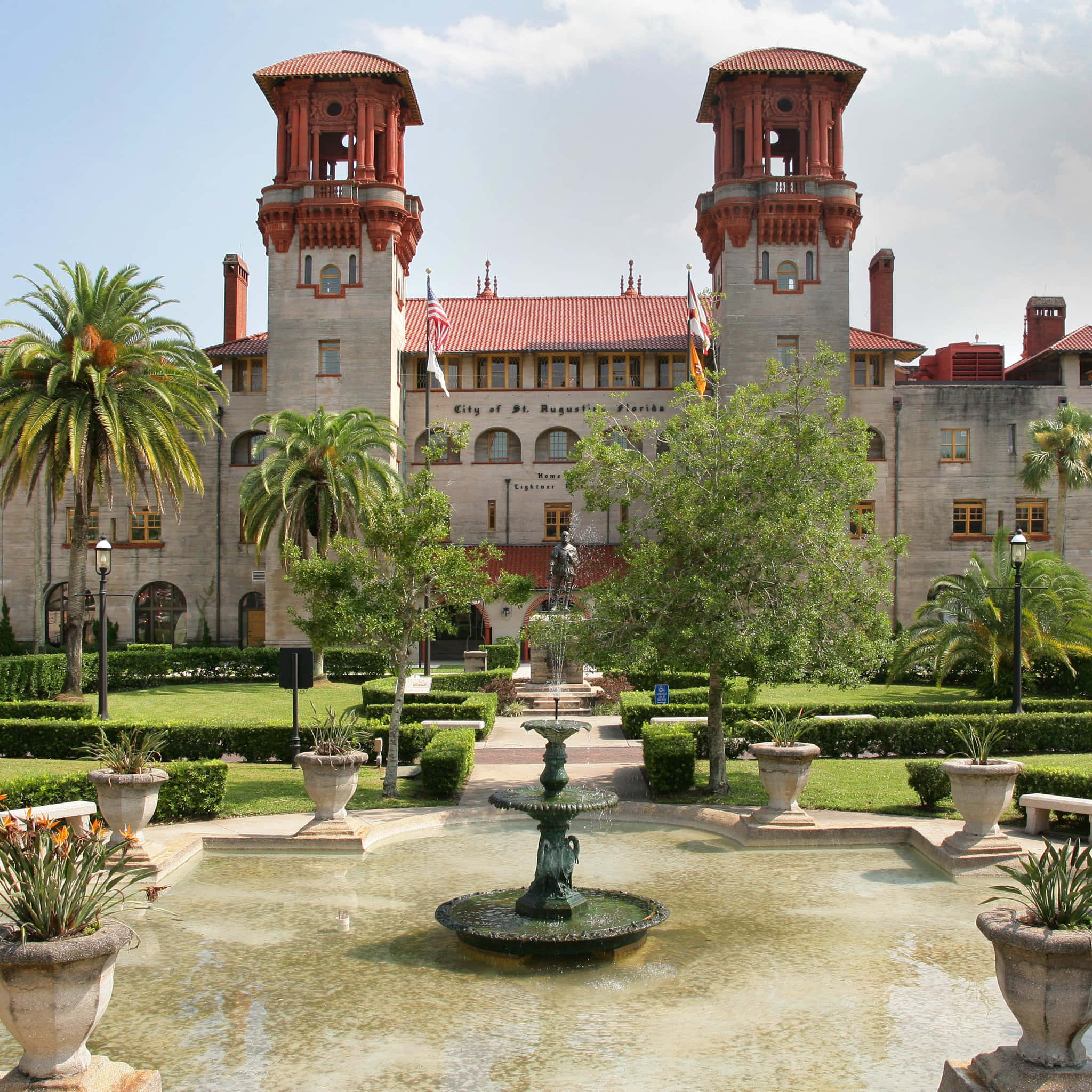 St Augustine Florida 桌布 壁紙 — 一座宏偉的歷史建築，擁有紅色瓦片塔樓和修剪整齊的花園，在明亮的藍天下設有中央噴泉。