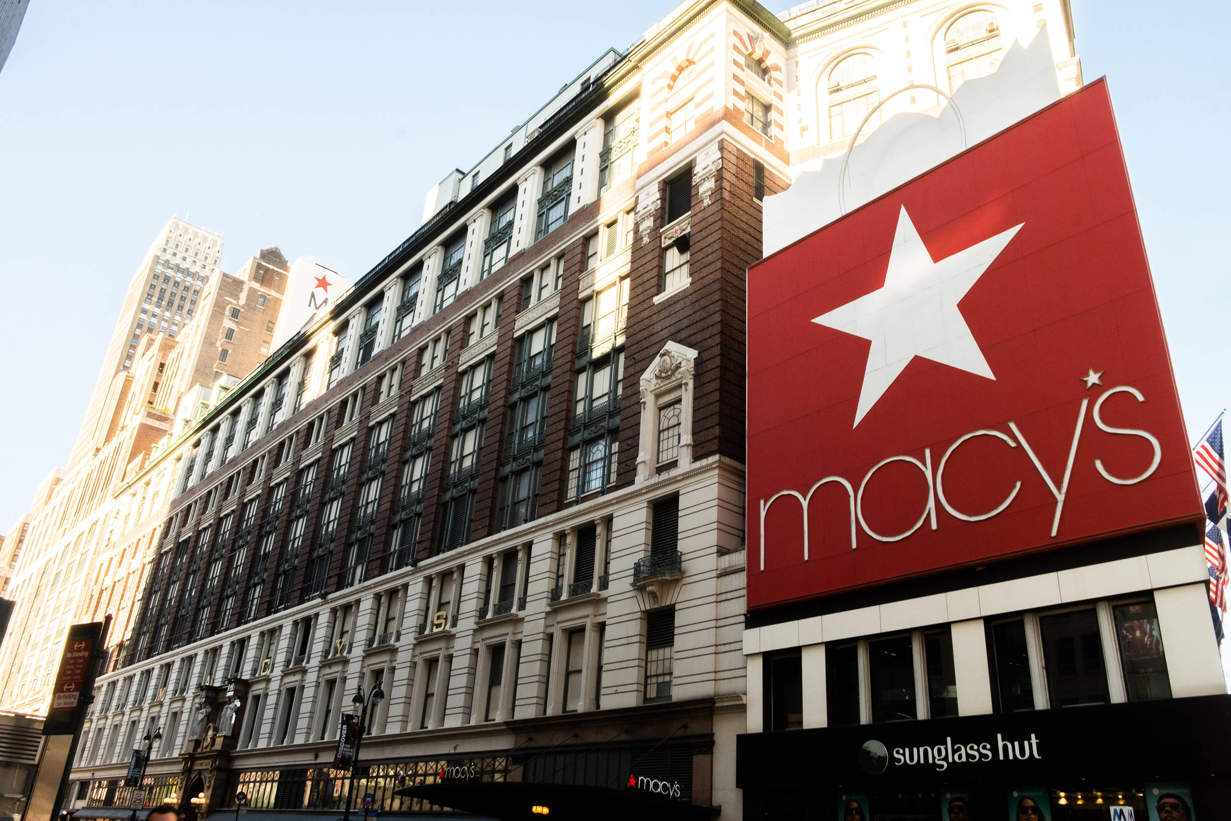 macys 桌布 壁紙 — 一座宏偉的歷史悠久的 Macy's 百貨公司大樓，在明亮的白天天空下有一個巨大的紅色星星標誌。