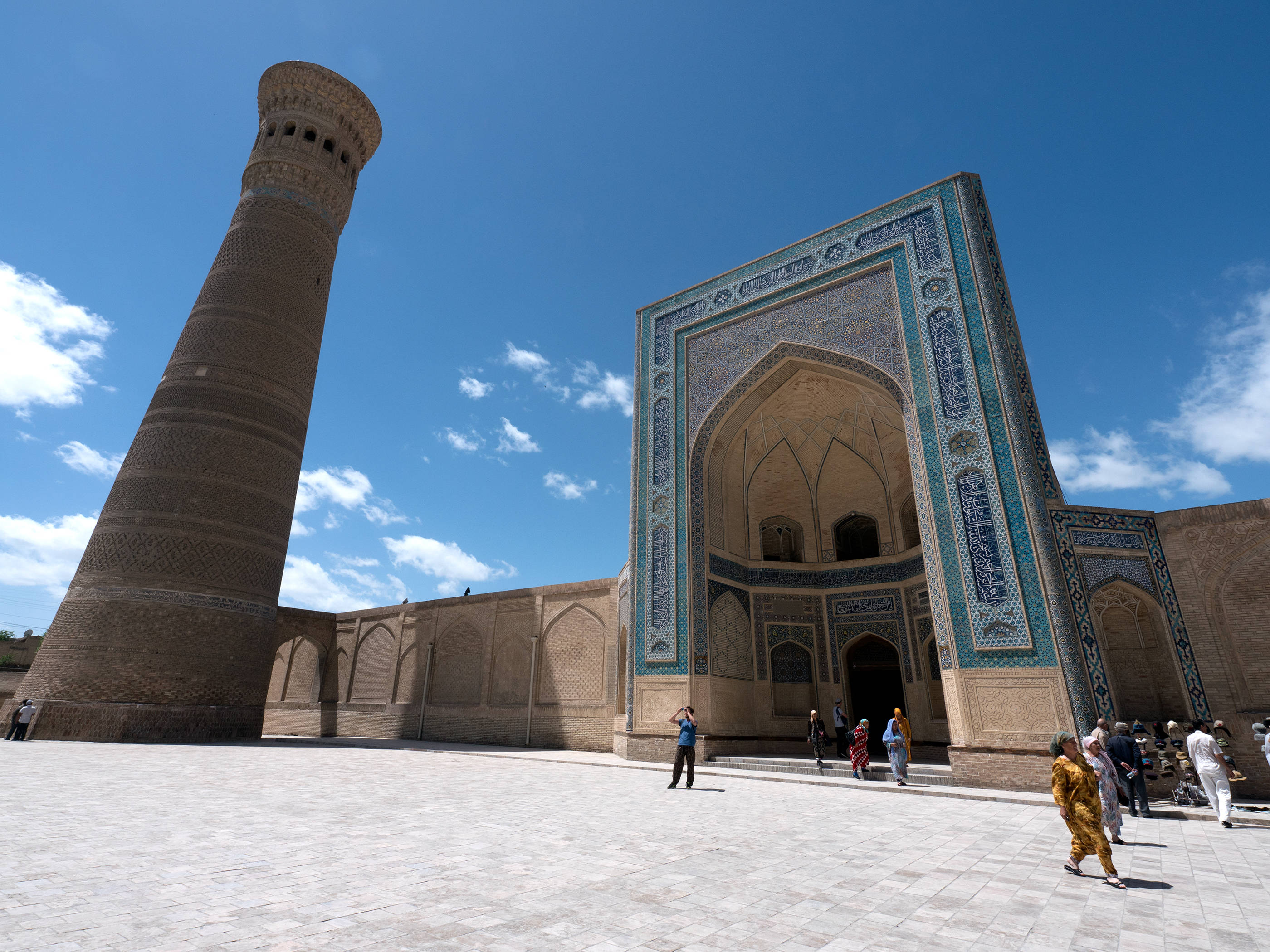 Uzbekistan 桌布 壁紙 — 一座宏偉的歷史清真寺，帶有複雜的藍色瓷磚工藝，矗立在高磚砌宣禮塔旁，天空湛藍，雲朵稀疏。