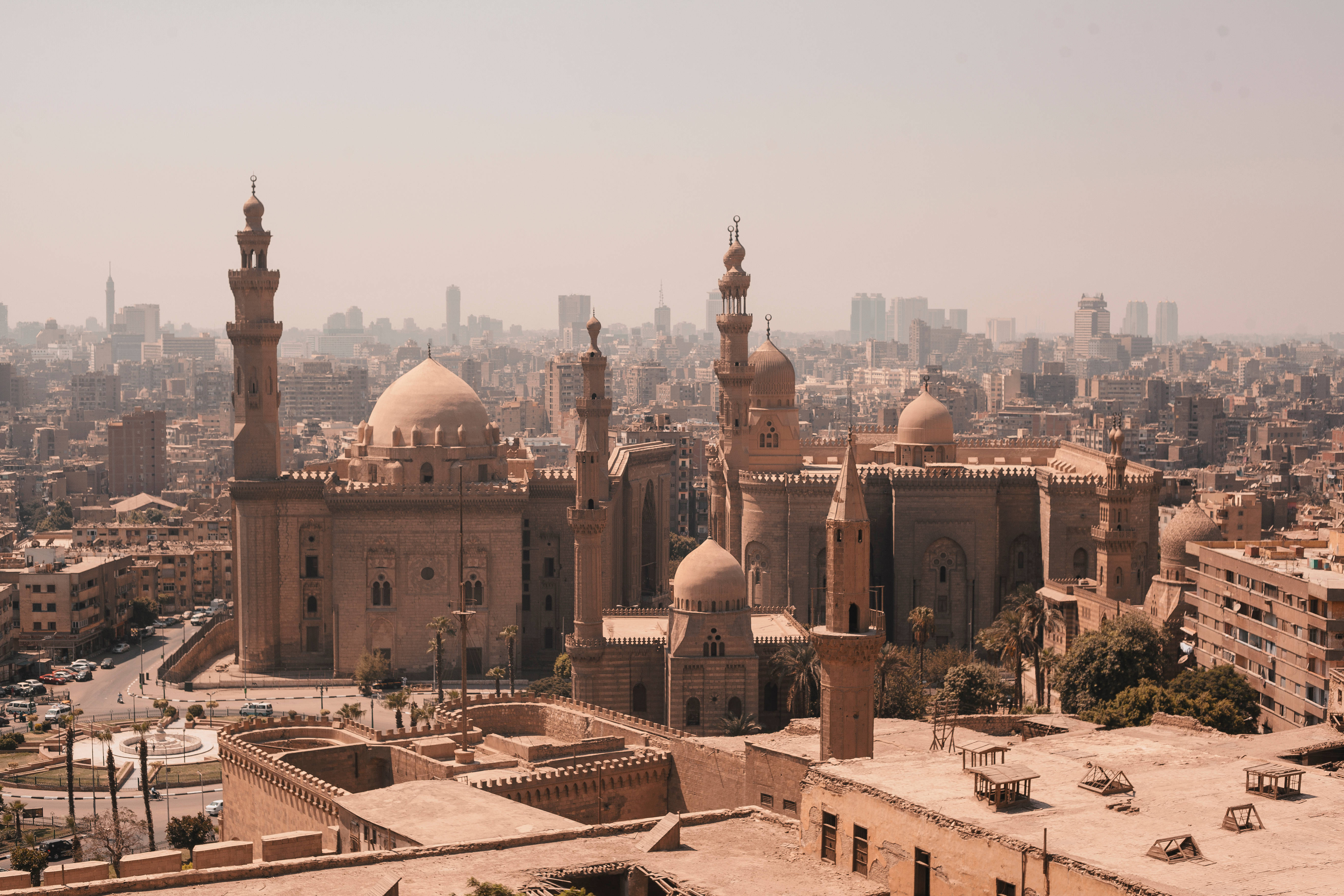 Egypt 桌布 壁紙 — 一座宏偉的歷史清真寺，擁有圓頂和宣禮塔，在朦朧的日光下聳立於密集的城市天際線之上。