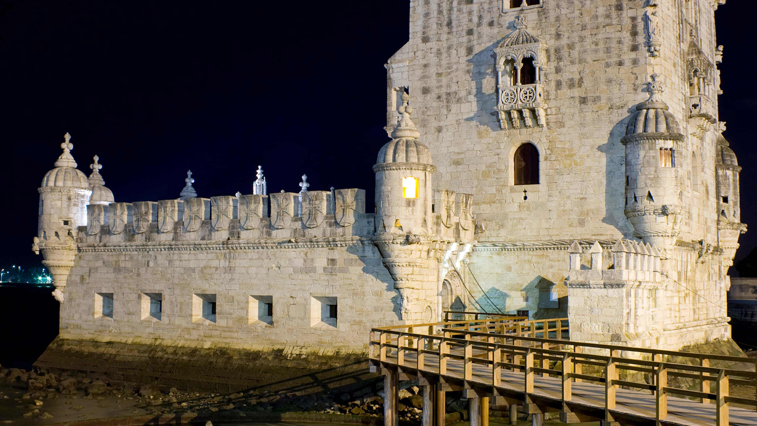 Portugal 桌布 壁紙 — 一座宏偉的歷史石塔和堡壘在夜間被溫暖的燈光照亮，映襯著黑暗的天空。