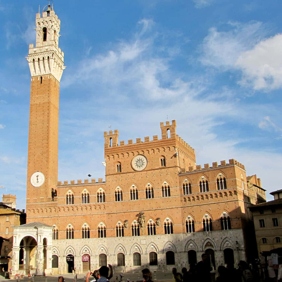 Piazza Del Campo 桌布 壁紙 — 一座宏偉的歷史磚砌建築，帶有高聳的鐘樓，矗立在晴朗的藍天和零星白雲下。