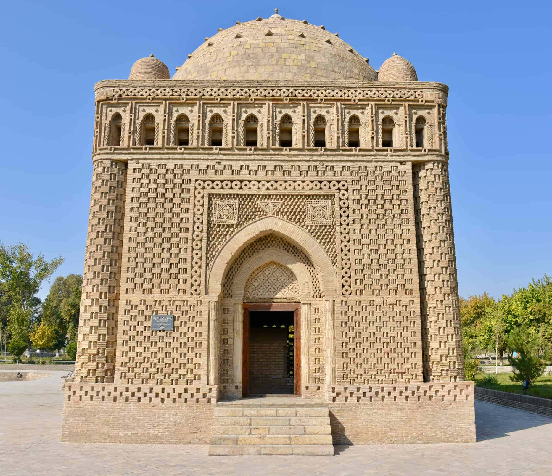 Uzbekistan 桌布 壁紙 — 一座宏偉的歷史陵墓，擁有精緻的磚砌結構和圓頂屋頂，矗立在晴朗的藍天下，四周樹木環繞。