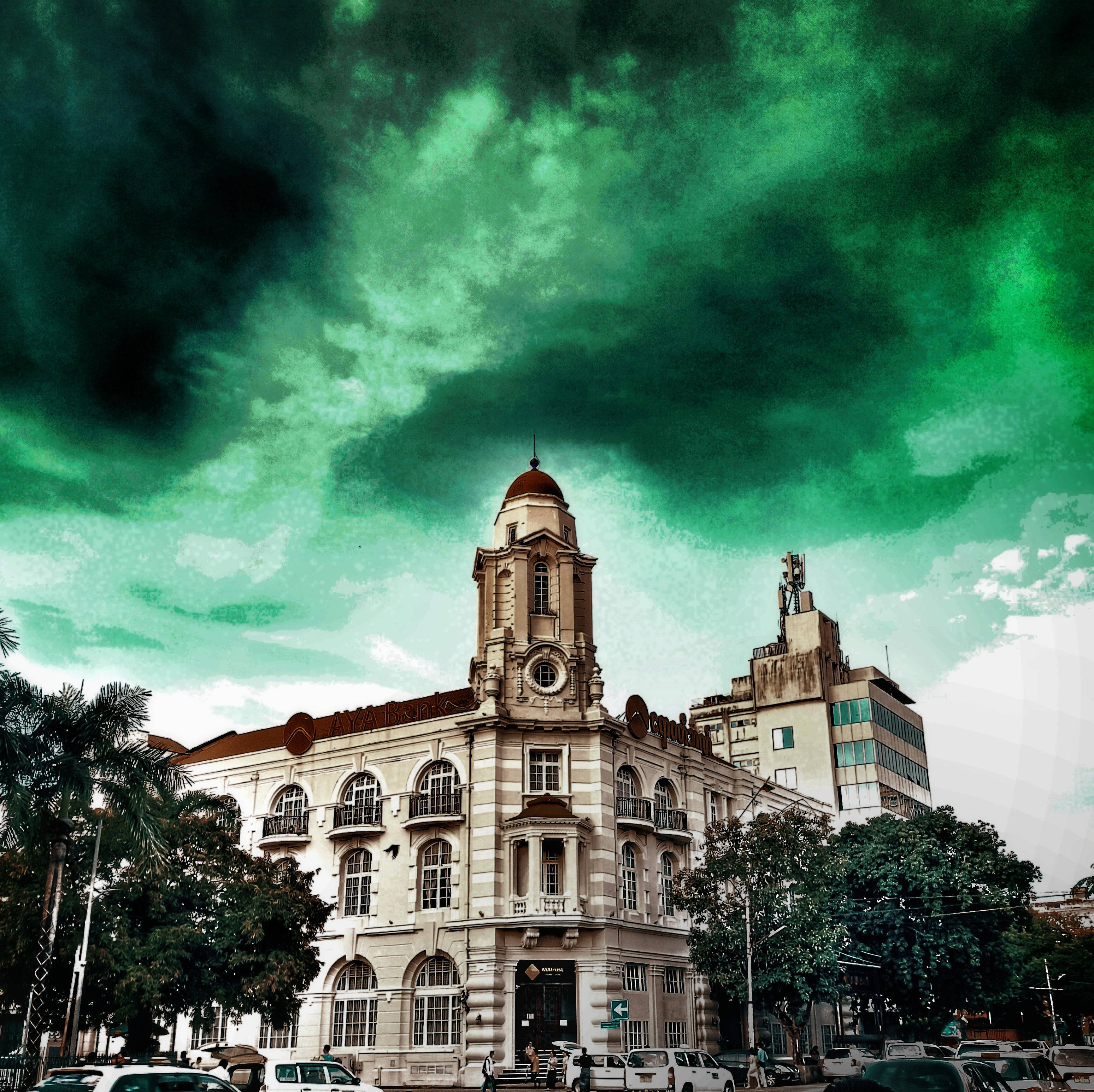 Yangon 桌布 壁紙 — 一座宏偉的殖民風格建築，帶有鐘樓，矗立在超現實的翡翠綠色天空下，天空佈滿戲劇性的雲彩。