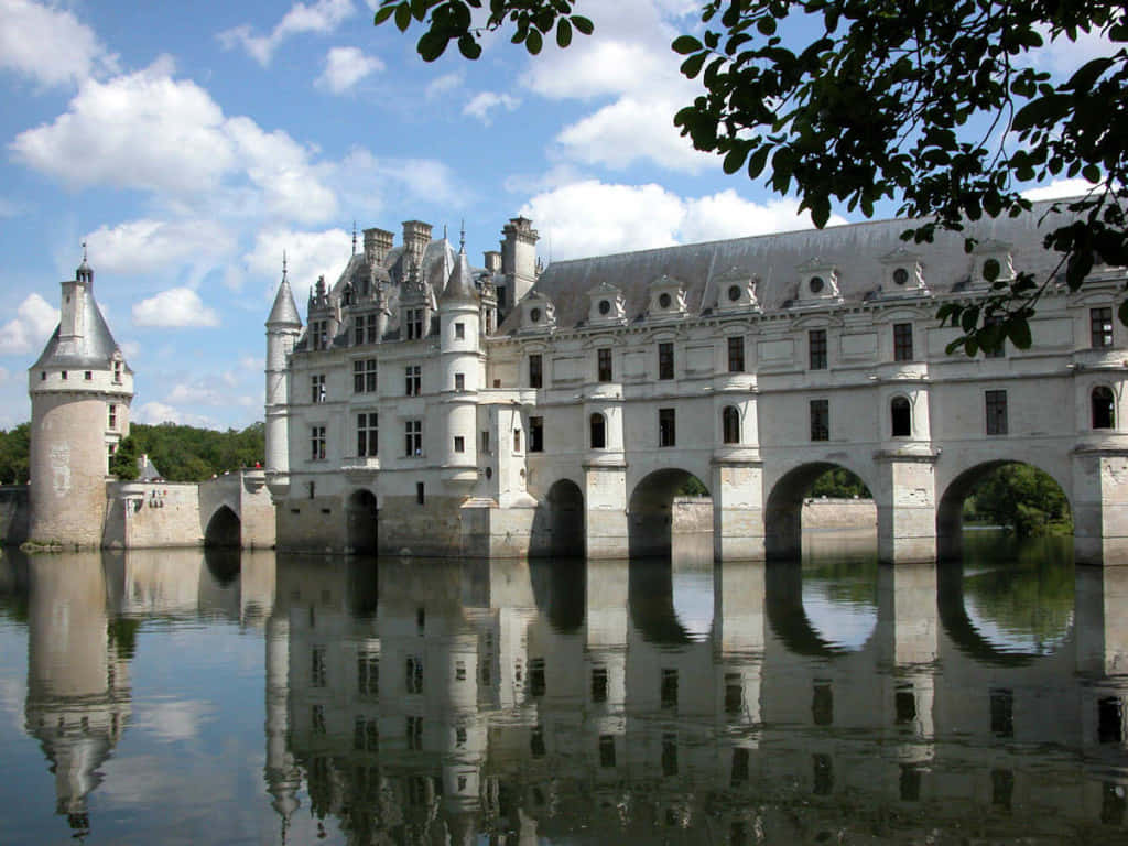 France 桌布 壁紙 — 一座宏偉的法國城堡，擁有石塔和拱橋，在晴朗藍天和蓬鬆白雲下，完美倒映在平靜的水面上。