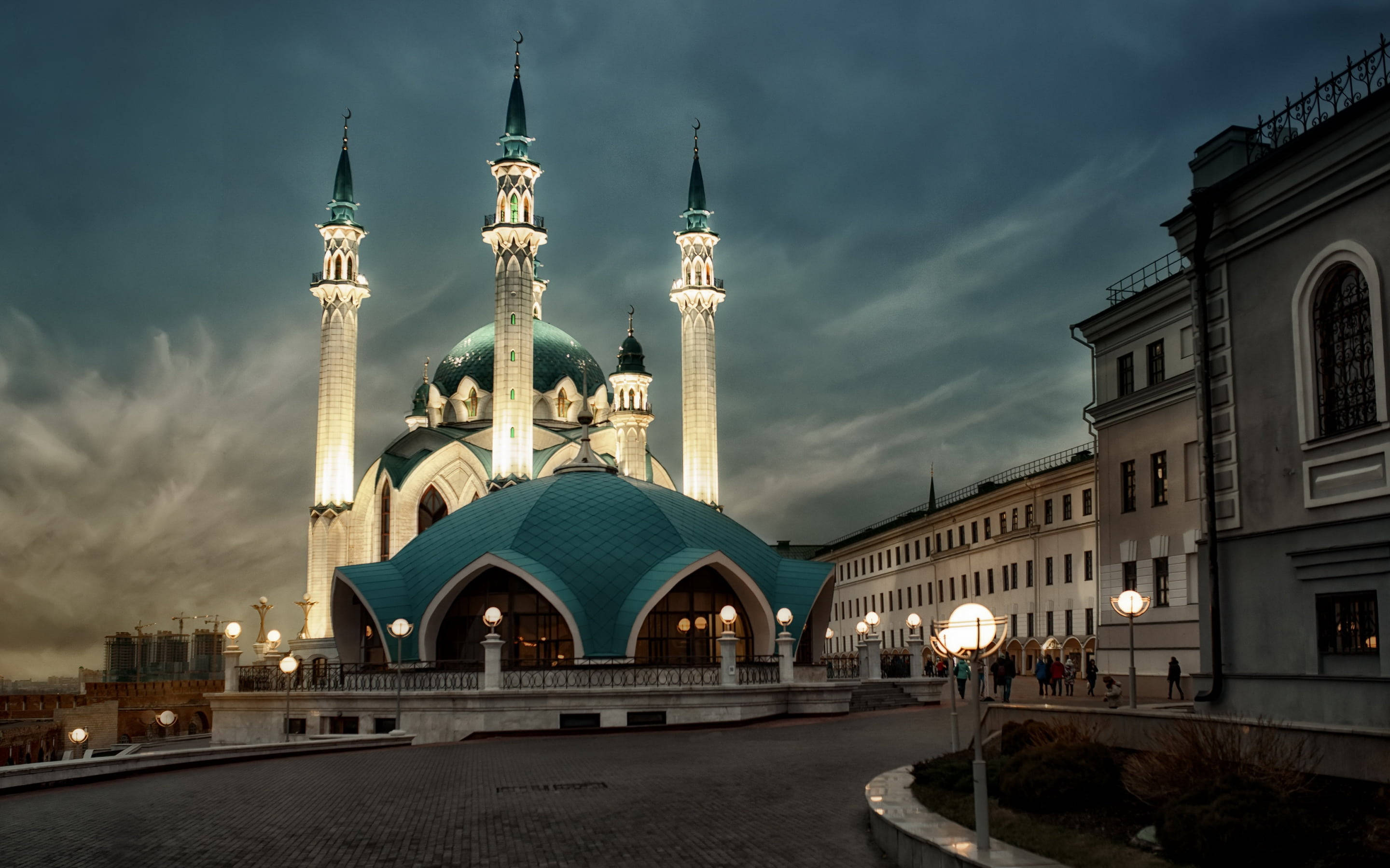 Madina Full HD 桌布 壁紙 — 一座宏偉的清真寺，帶有發光的綠松石圓頂和宣禮塔，在陰沉的暮色天空下熠熠生輝。
