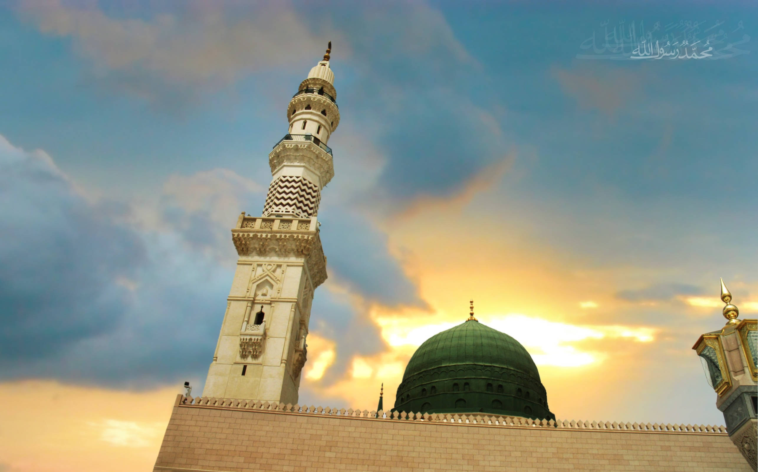 Madina Sharif 桌布 壁紙 — 一座宏偉的清真寺，擁有綠色圓頂和華麗的白色宣禮塔，在戲劇性的日落天空下聳立。