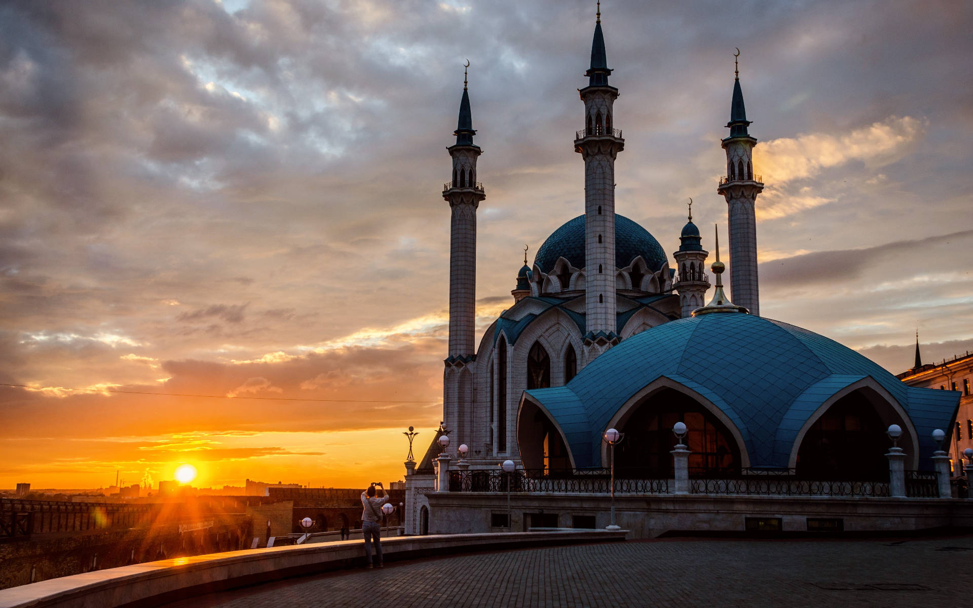 Kazan 桌布 壁紙 — 一座宏偉的清真寺，擁有藍色圓頂和宣禮塔，在戲劇性的多雲天空下沐浴在金色的日落光芒中。