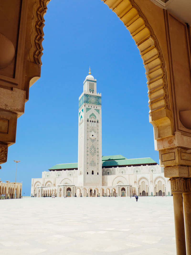 Mosque 桌布 壁紙 — 一座宏偉的清真寺，高聳的宣禮塔被華麗的石拱門框住，襯著清澈的藍天。