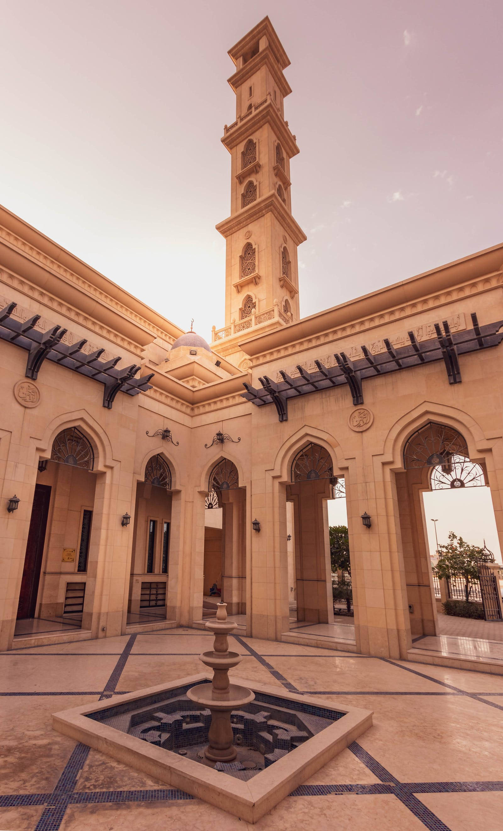 HD Islamic 桌布 壁紙 — 一座宏偉的清真寺庭院，中央有噴泉和高聳的宣禮塔，沐浴在溫暖的黃金時刻光線中。