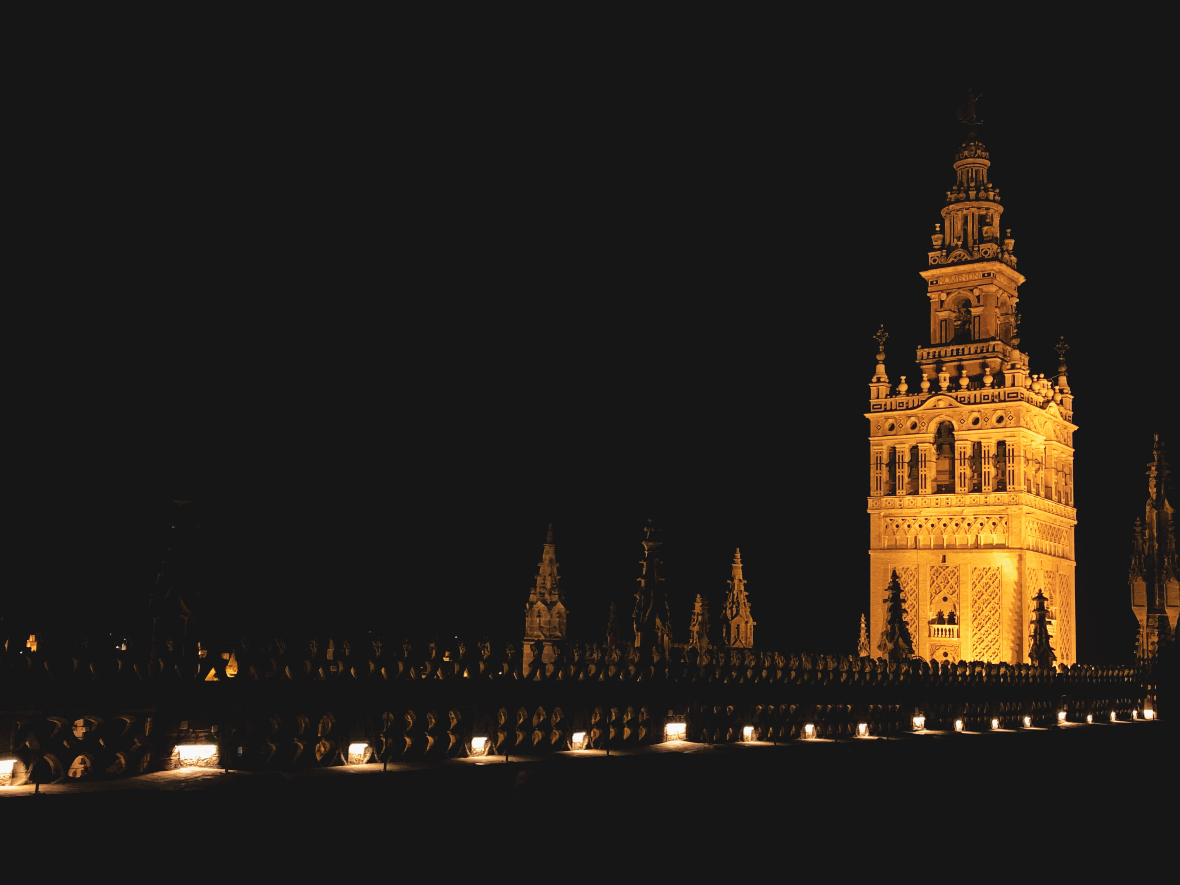 Seville 桌布 壁紙 — 一座宏偉的照明塔在漆黑的夜空中溫暖地發光，下方有一排發光的燈籠。