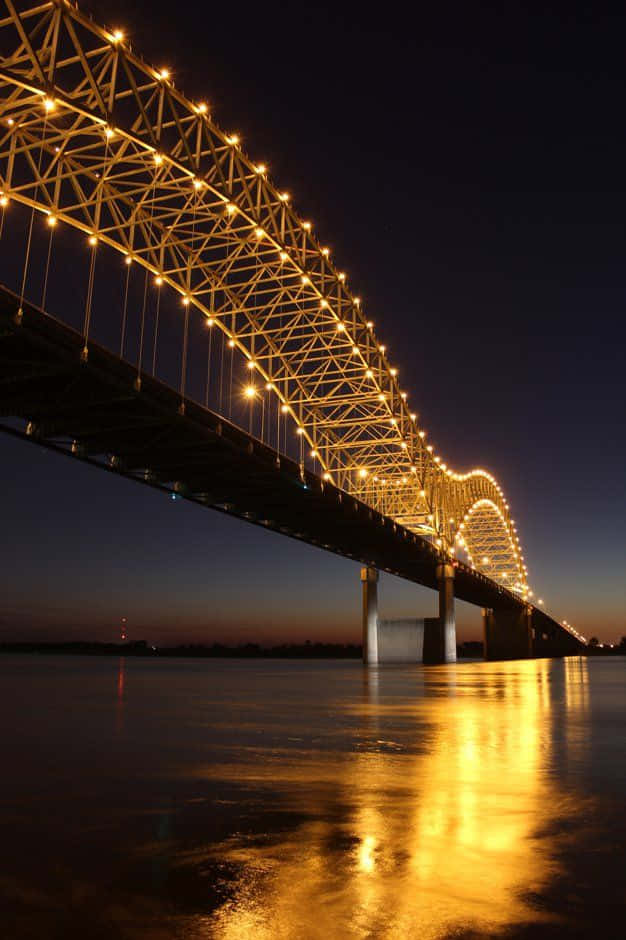 bridge 桌布 壁紙 — 一座宏偉的照明桁架橋在黃昏時分拱跨平靜的河流，在水面上投下金色的倒影。