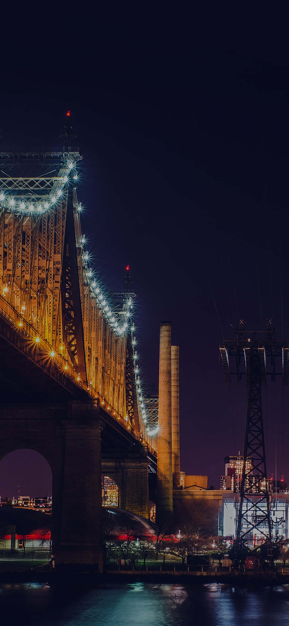 New York City Night iPhone 桌布 壁紙 — 一座宏偉的照明橋樑在深邃的夜空中溫暖地發光，城市燈光倒映在下方平靜的水面上。