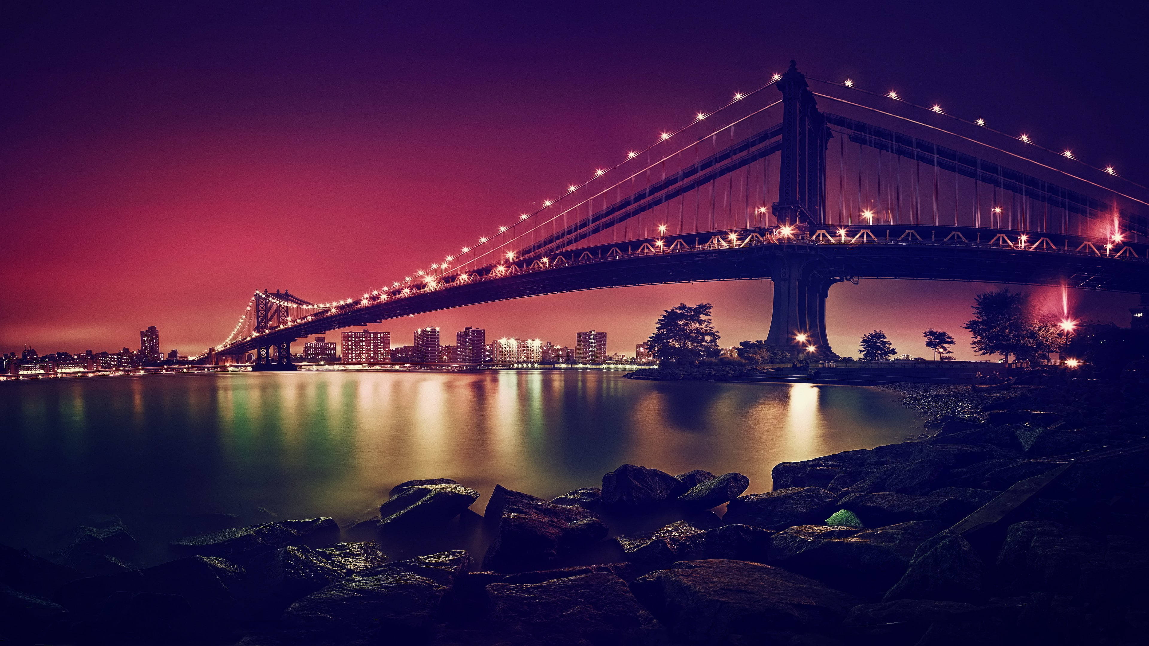 New York 桌布 壁紙 — 一座宏偉的照明橋樑橫跨平靜的水道，在暮色中，充滿活力的紫色和粉紅色天空倒映在水面上。