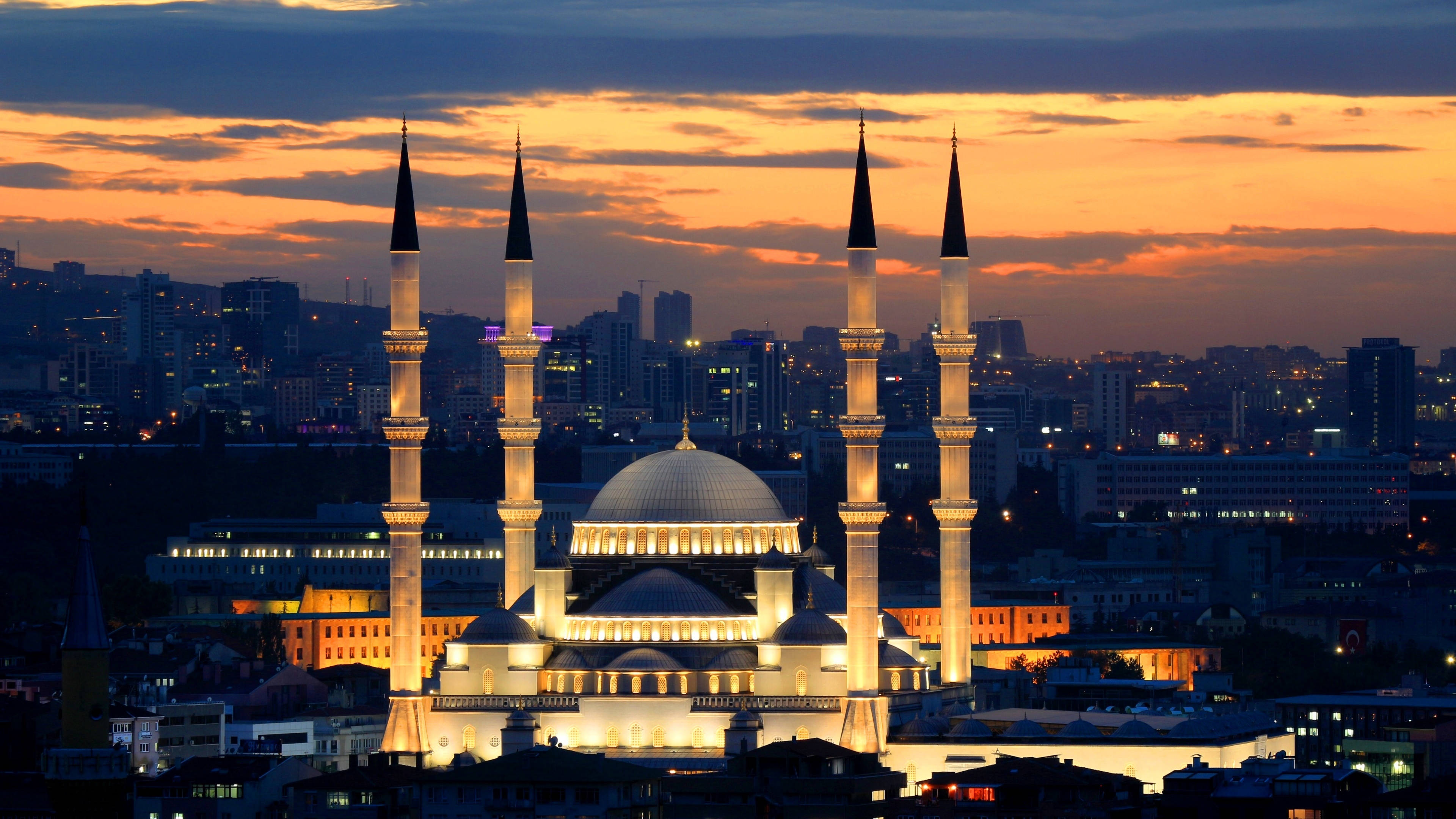 Ankara 桌布 壁紙 — 一座宏偉的燈光清真寺，擁有四座宣禮塔，在充滿活力的橙色和紫色暮色天空中雄偉地聳立於廣闊的城市景觀之上。
