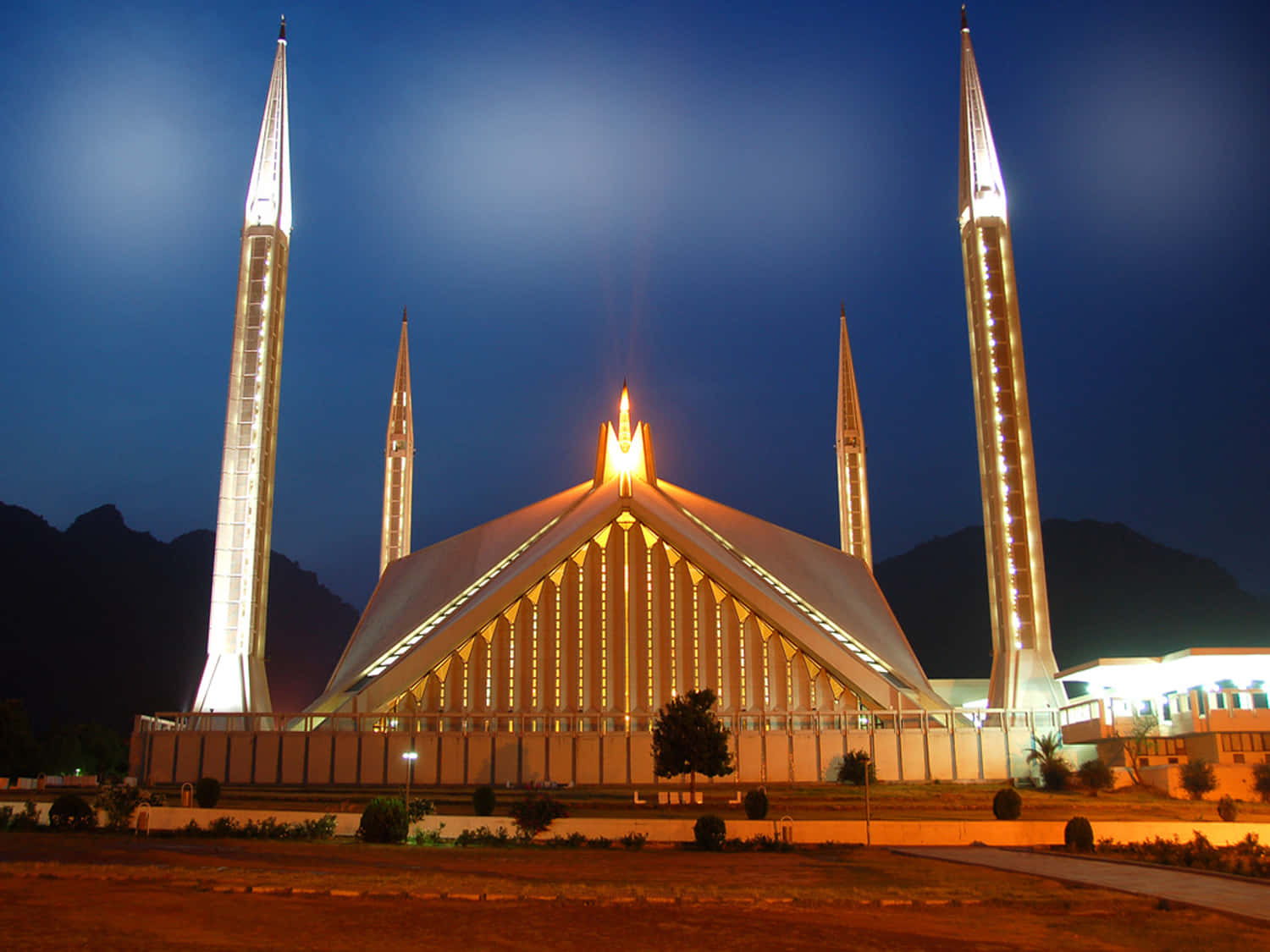 Pakistan 桌布 壁紙 — 一座宏偉的燈光清真寺，擁有四座高聳的宣禮塔，在深藍色的暮色天空中溫暖地發光。