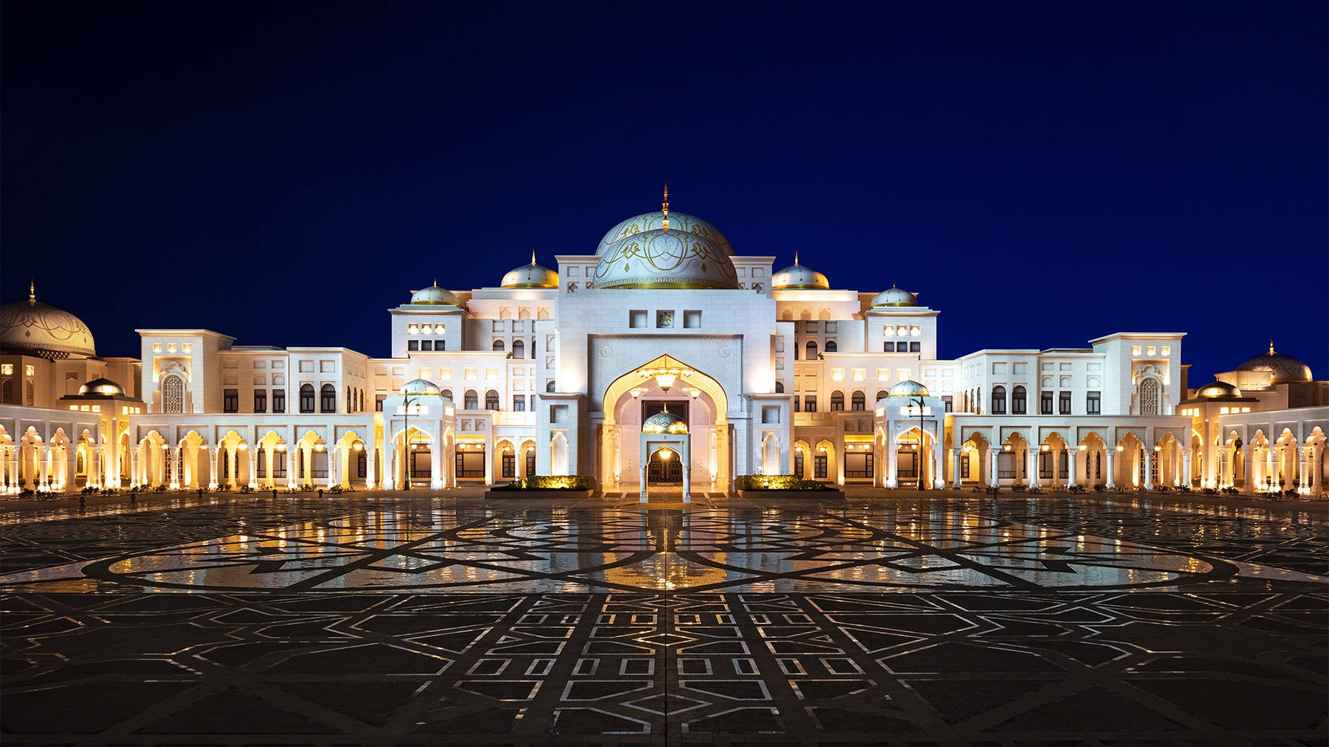 Arab 桌布 壁紙 — 一座宏偉的燈光清真寺，擁有金色圓頂和拱形入口，在深藍色夜空下美麗地倒映在濕潤的瓷磚廣場上。