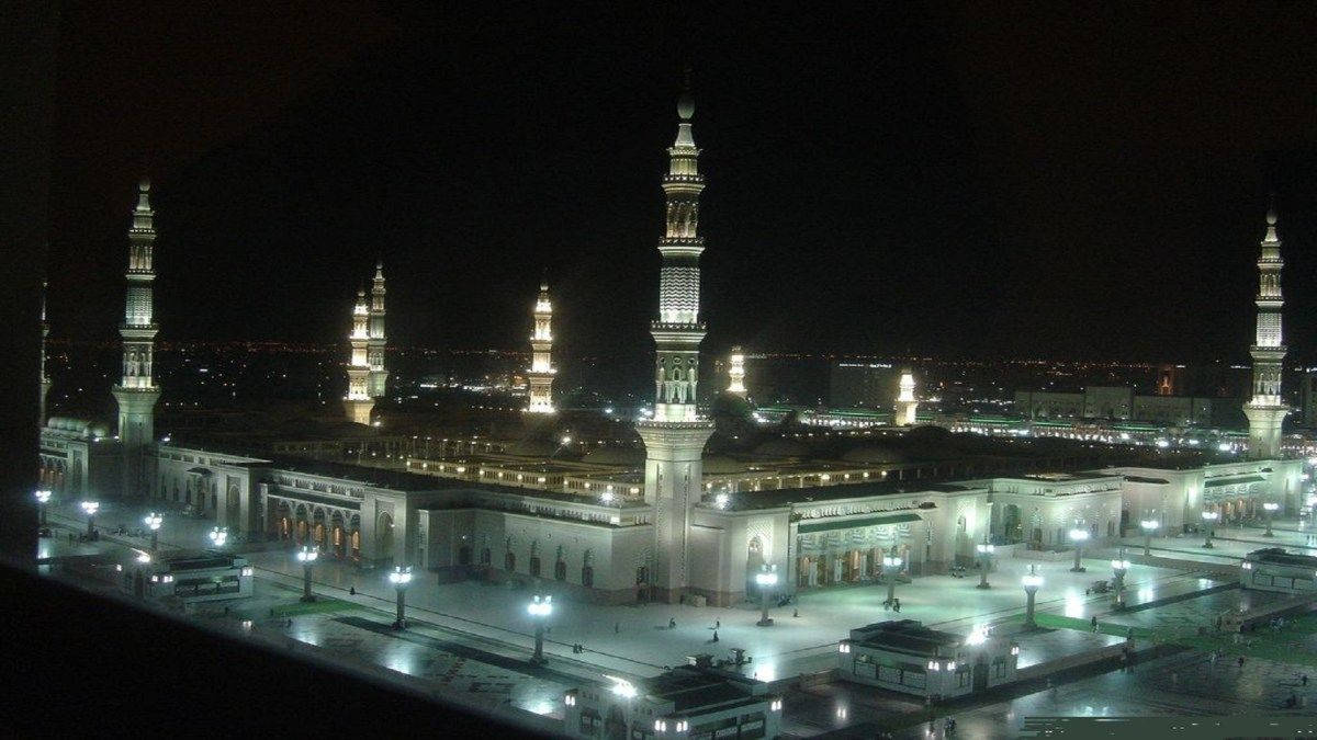 Madina Sharif 桌布 壁紙 — 一座宏偉的燈光清真寺，有多個宣禮塔，在夜空下巍然聳立，庭院沐浴在溫暖的人造燈光中。