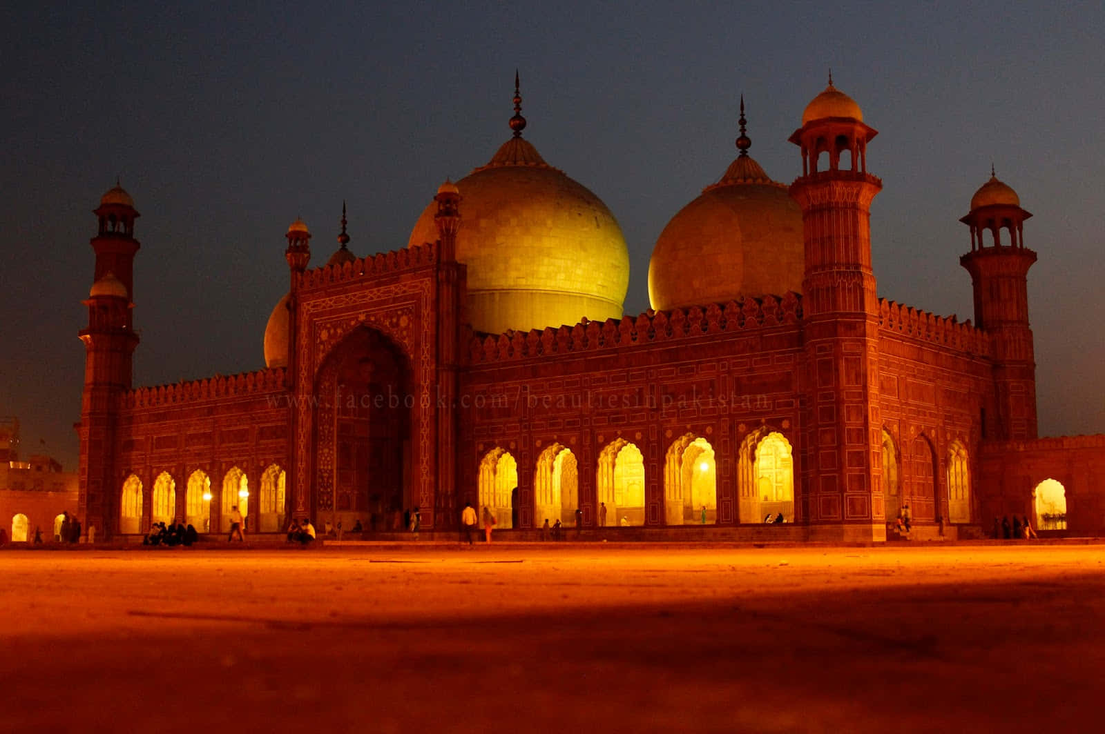 Pakistan 桌布 壁紙 — 一座宏偉的燈光清真寺，金色圓頂和紅色砂岩拱門在深沉的暮色天空中溫暖地發光。