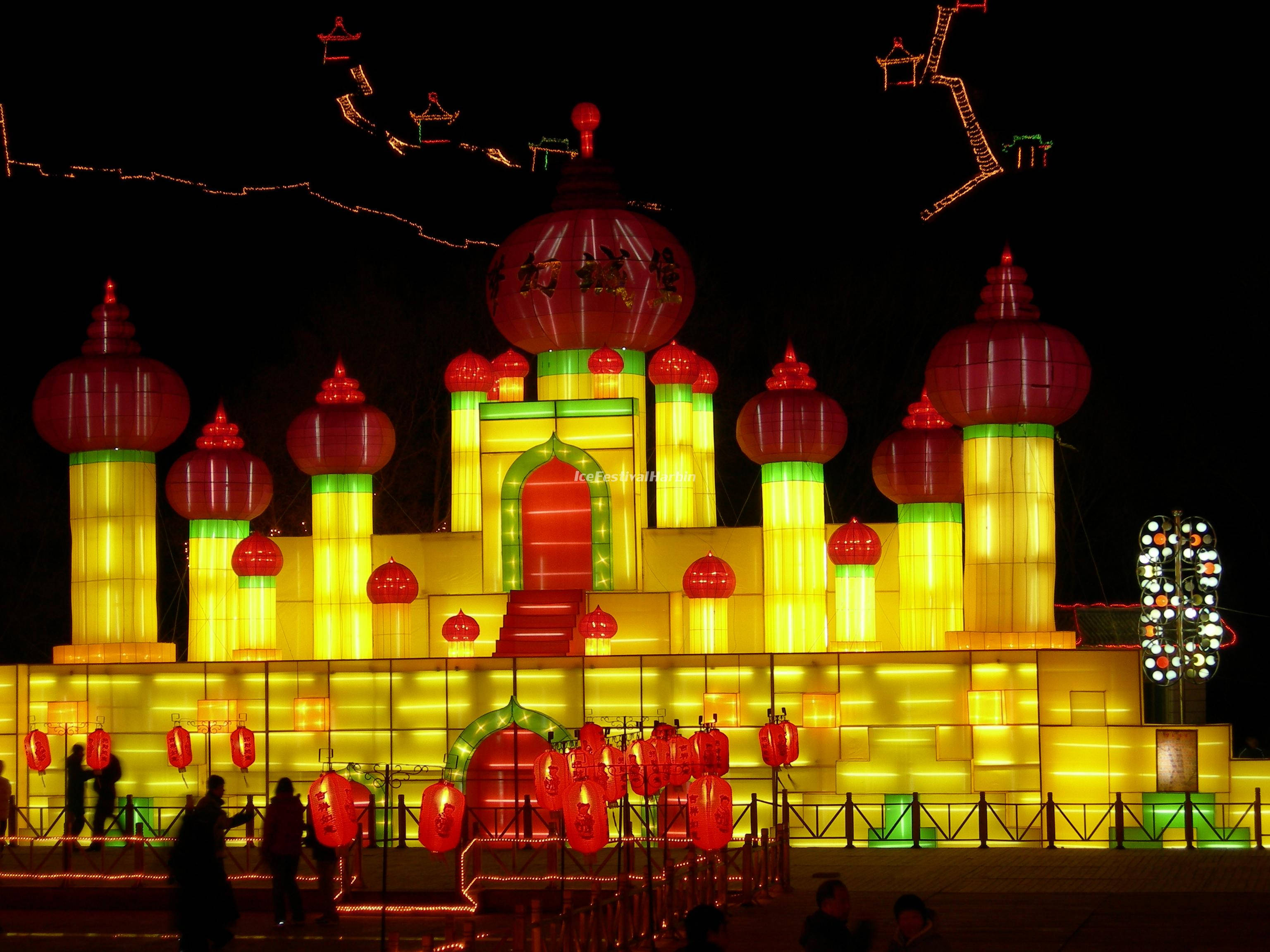 Harbin 桌布 壁紙 — 一座宏偉的燈籠城堡在漆黑的夜空下閃耀著鮮豔的紅黃燈光，剪影般的遊客欣賞著節日展示。