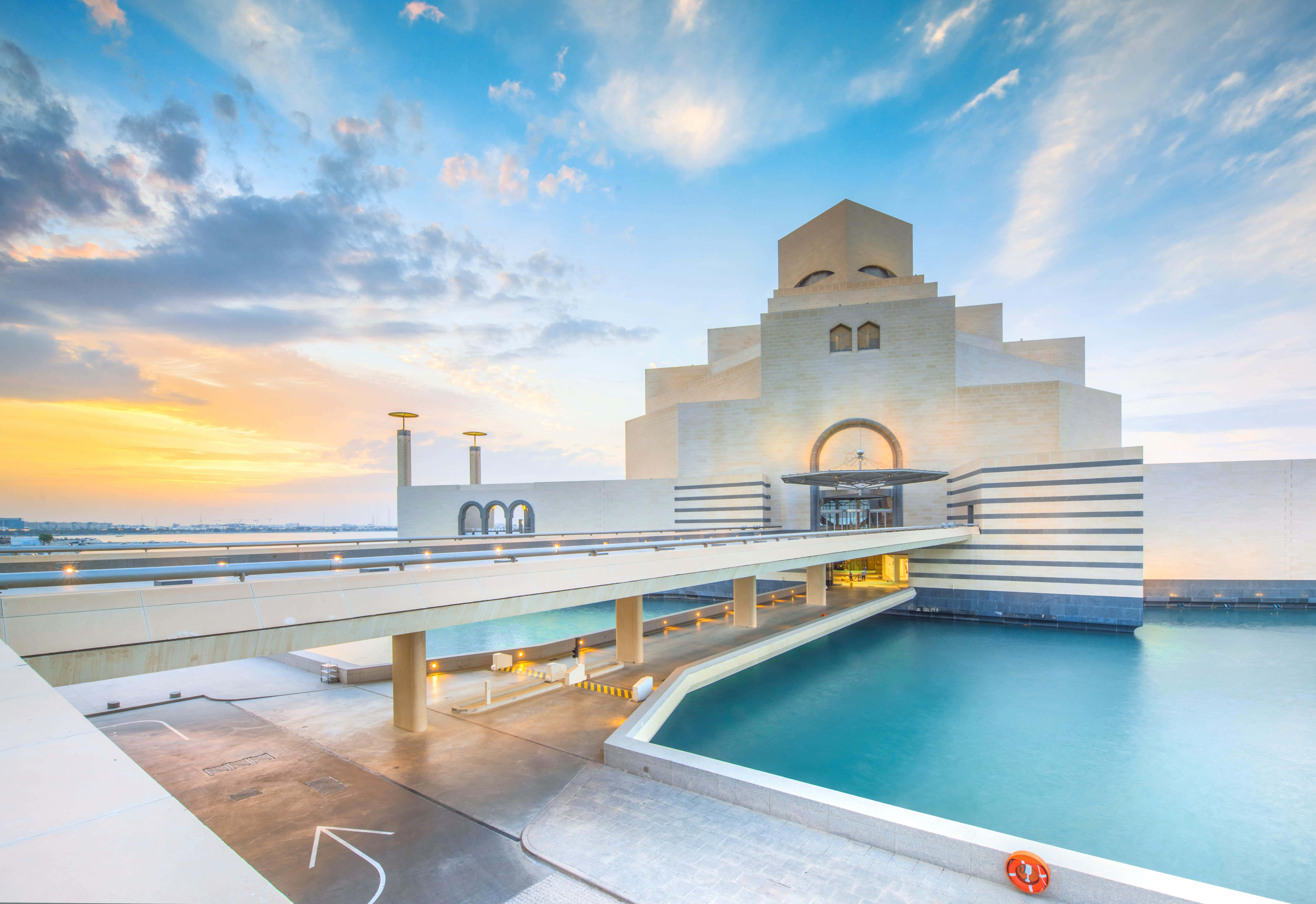 Museum Of Islamic Art 桌布 壁紙 — 一座宏偉的現代博物館，採用幾何建築風格，矗立在碧綠的泳池旁，映襯著 vibrant 的日落天空。