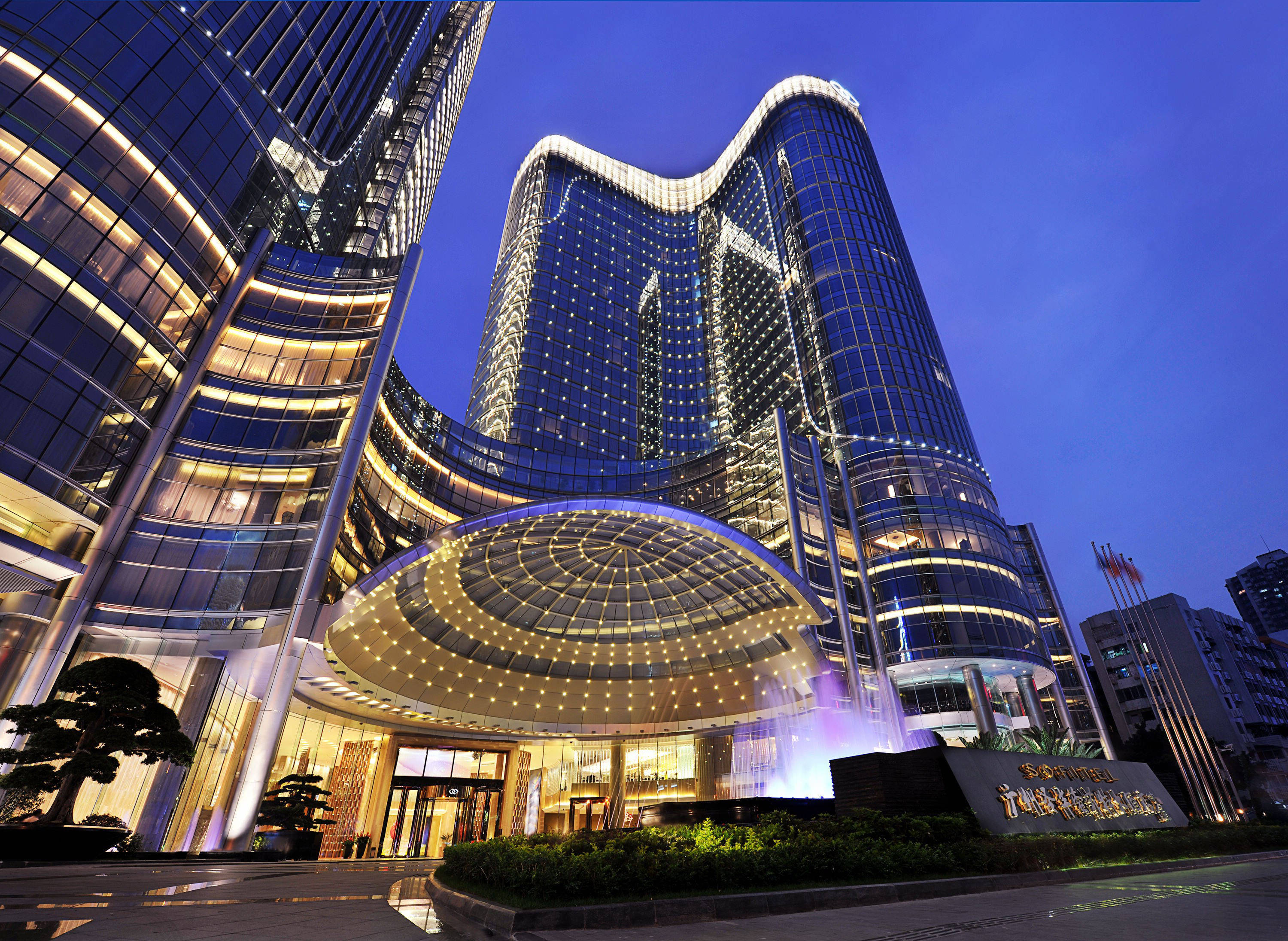 Guangzhou 桌布 壁紙 — 一座宏偉的現代飯店，擁有弧形玻璃塔和閃爍的燈光，在暮色天空下巍然聳立。