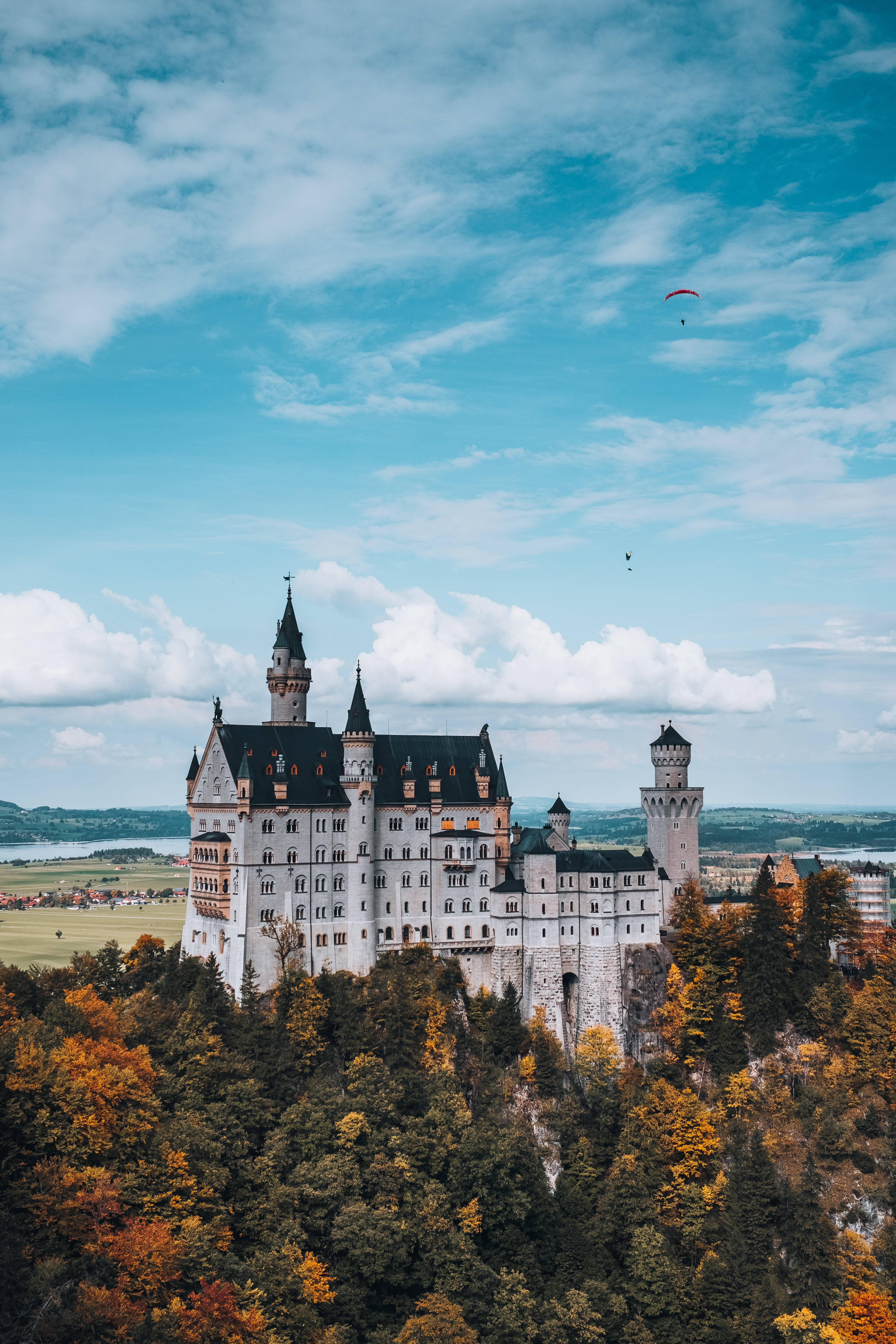 Neuschwanstein Castle 桌布 壁紙 — 一座宏偉的白色城堡，黑色屋頂，坐落在樹木繁茂的山丘上，天空湛藍，點綴著蓬鬆的白雲。