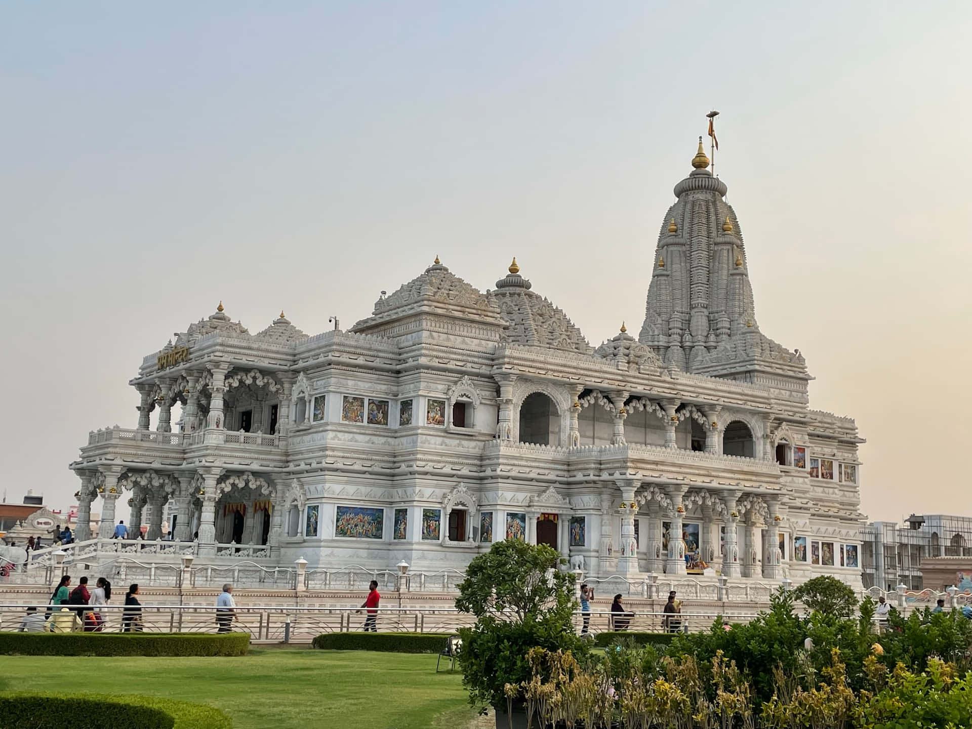 PREM TEMPLE BRINDAVAN OF KRISHNA 壁紙 — 一座宏偉的白色大理石寺廟，擁有金色尖頂和精緻雕刻，在柔和的天空下巍然聳立，遊客在附近漫步。
