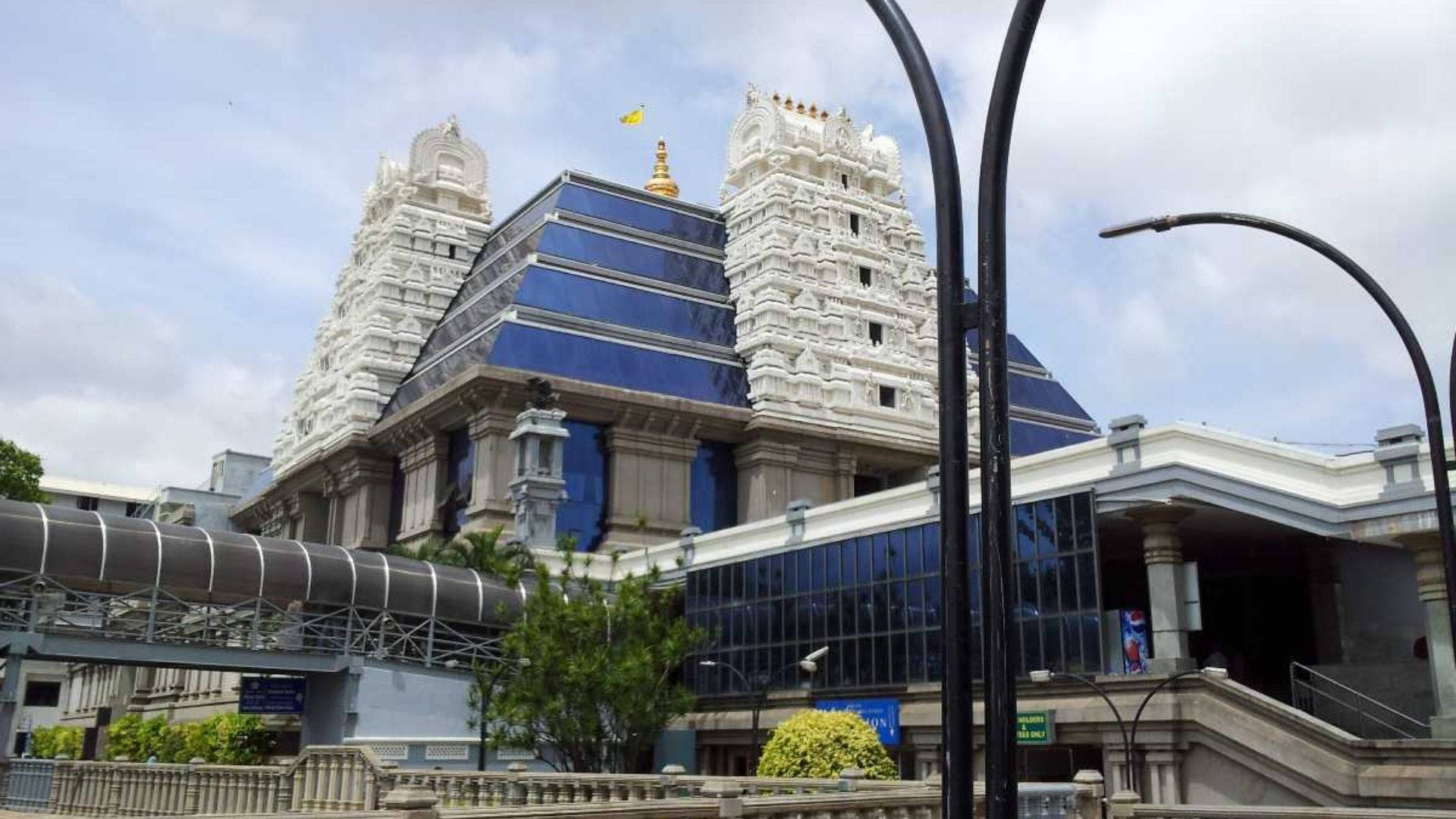 Bangalore 桌布 壁紙 — 一座宏偉的白色寺廟，帶有藍色玻璃屋頂塔樓，聳立在現代玻璃建築後面，天空多雲。