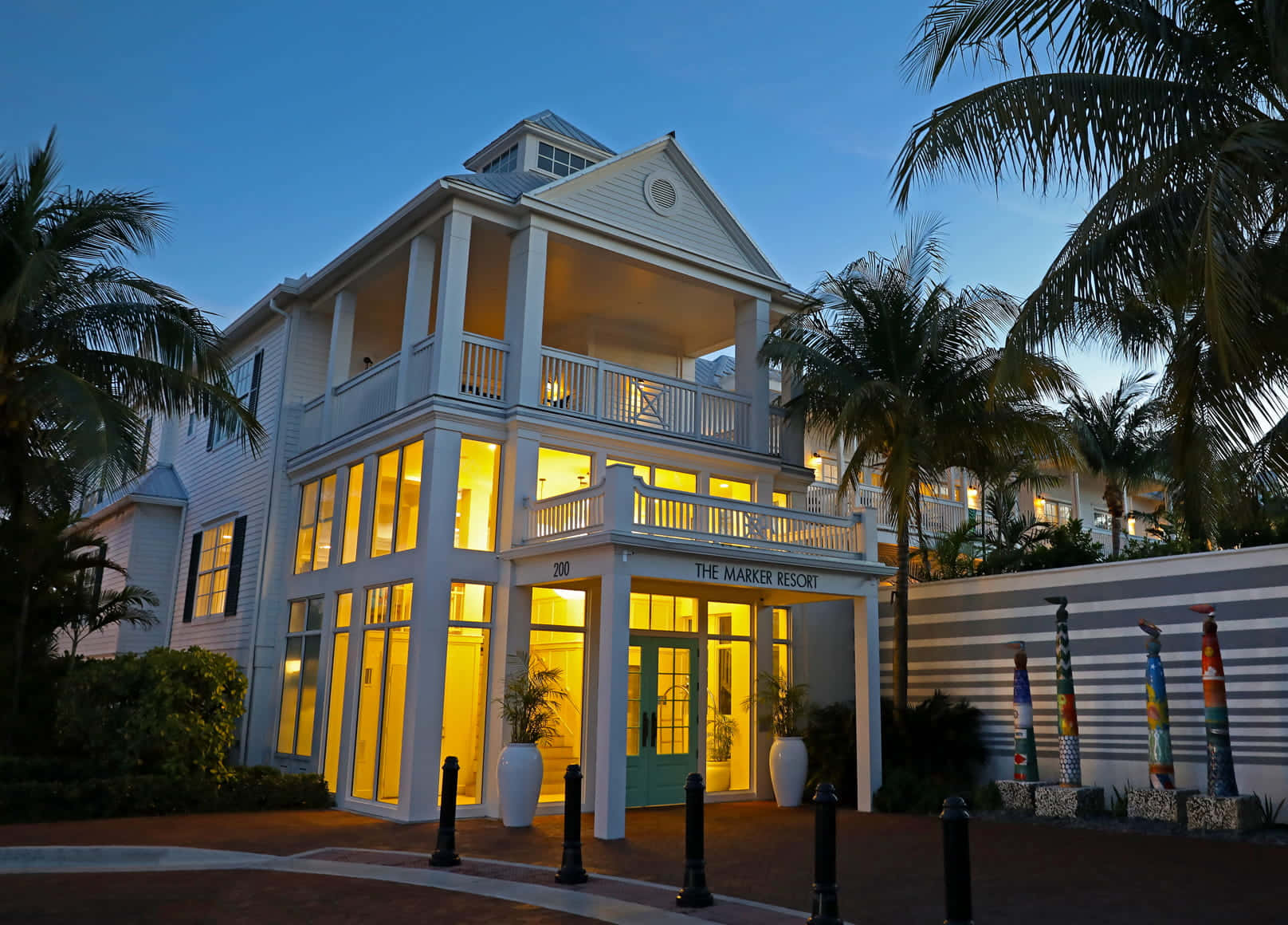 Key West 桌布 壁紙 — 一座宏偉的白色度假村建築在黃昏時分溫暖地發光，周圍環繞著棕櫚樹和色彩繽紛的雕塑。