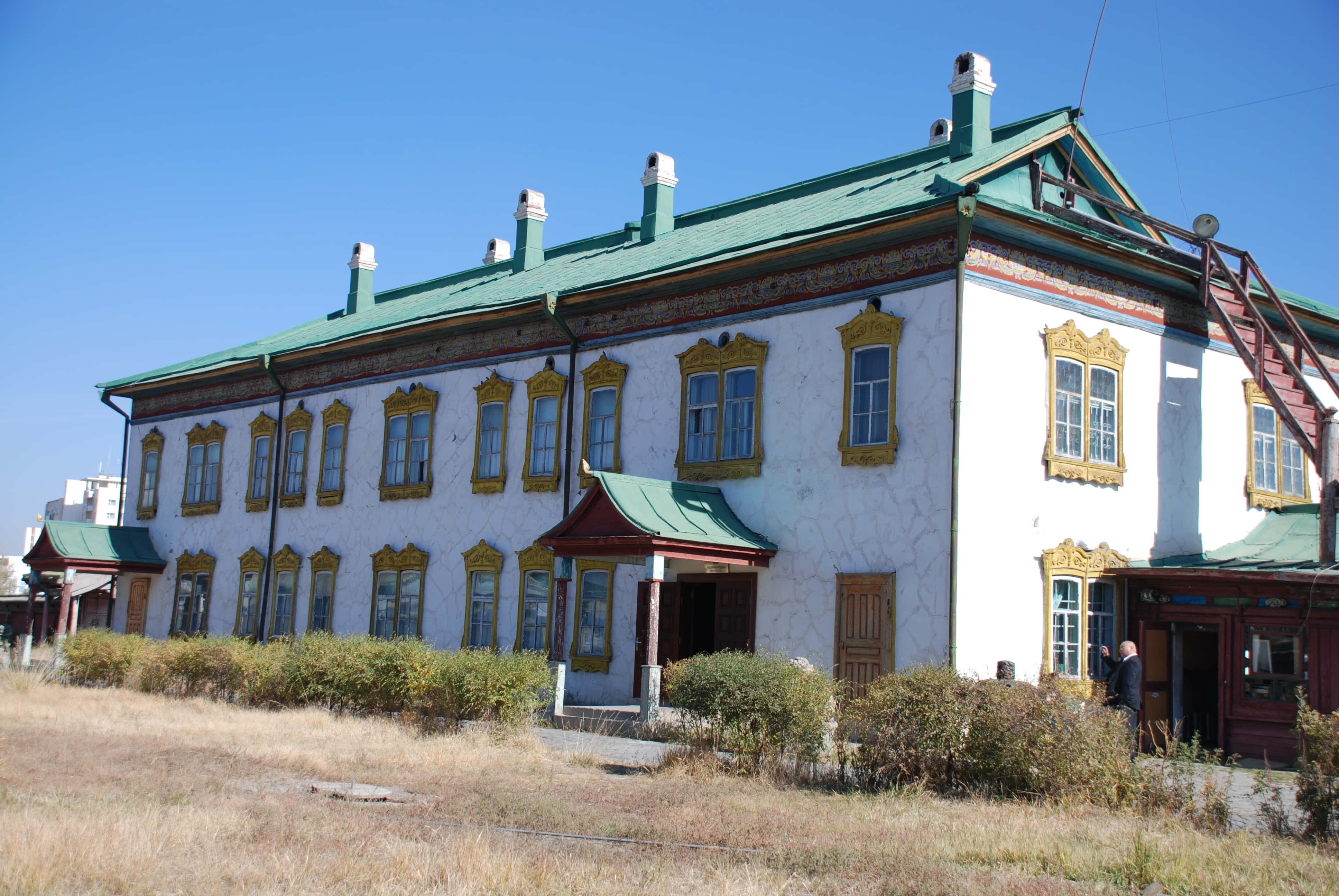 Mongolia 桌布 壁紙 — 一座宏偉的白色建築，帶有華麗的金色窗框和綠色屋頂，矗立在晴朗的藍天下，前景有乾草。