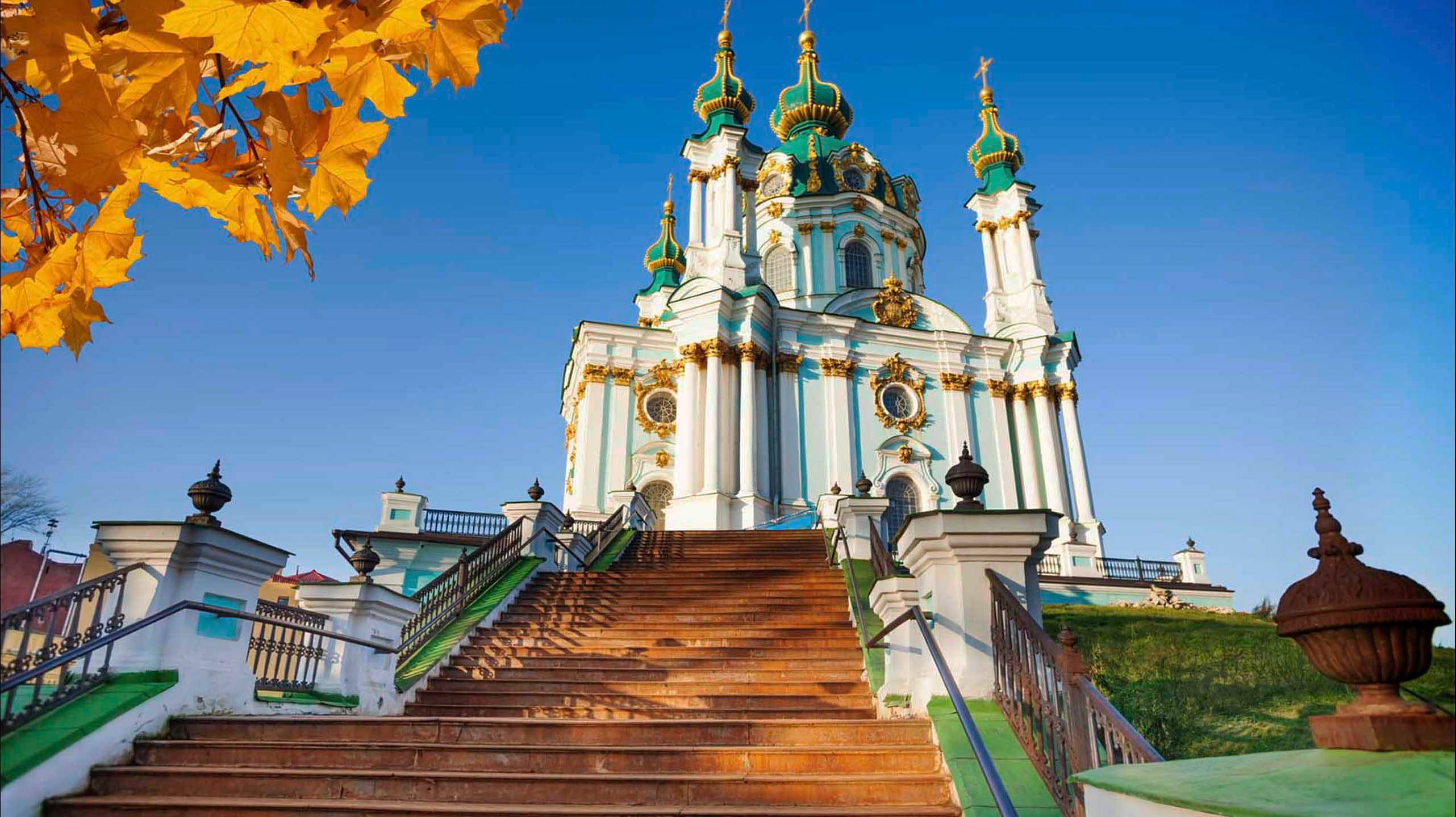Ukraine 桌布 壁紙 — 一座宏偉的白色教堂，帶有綠色圓頂，聳立在寬闊的石階之上，周圍環繞著金黃色的秋葉，在清澈的藍天下。