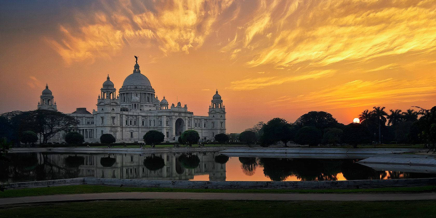 Kolkata 桌布 壁紙 — 一座宏偉的白色新古典主義建築在平靜的水面上倒映，天空是火熱的橙黃色日落。