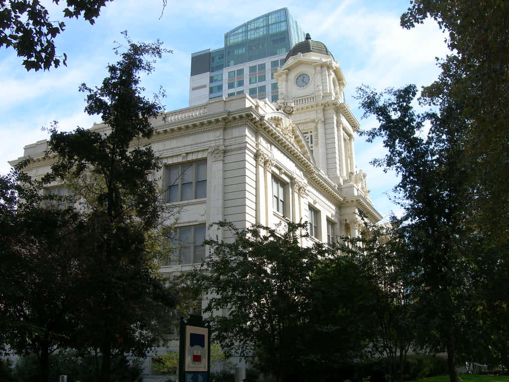 Clock 桌布 壁紙 — 一座宏偉的白色歷史法院建築，帶有鐘樓，在藍天白雲下被茂密的綠樹環繞。