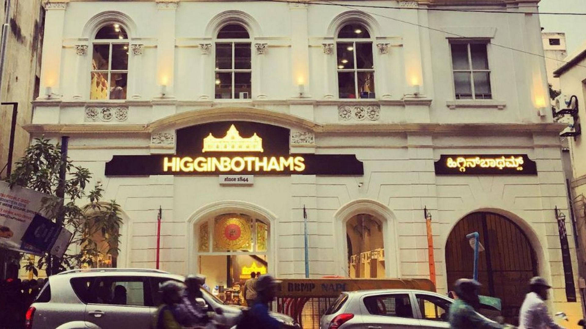 清奈 桌布 壁紙 — 一座宏偉的白色殖民風格建築，帶有 'HIGGINBOTHAMS' 發光招牌和拱形窗戶，街道交通和行人熙熙攘攘。