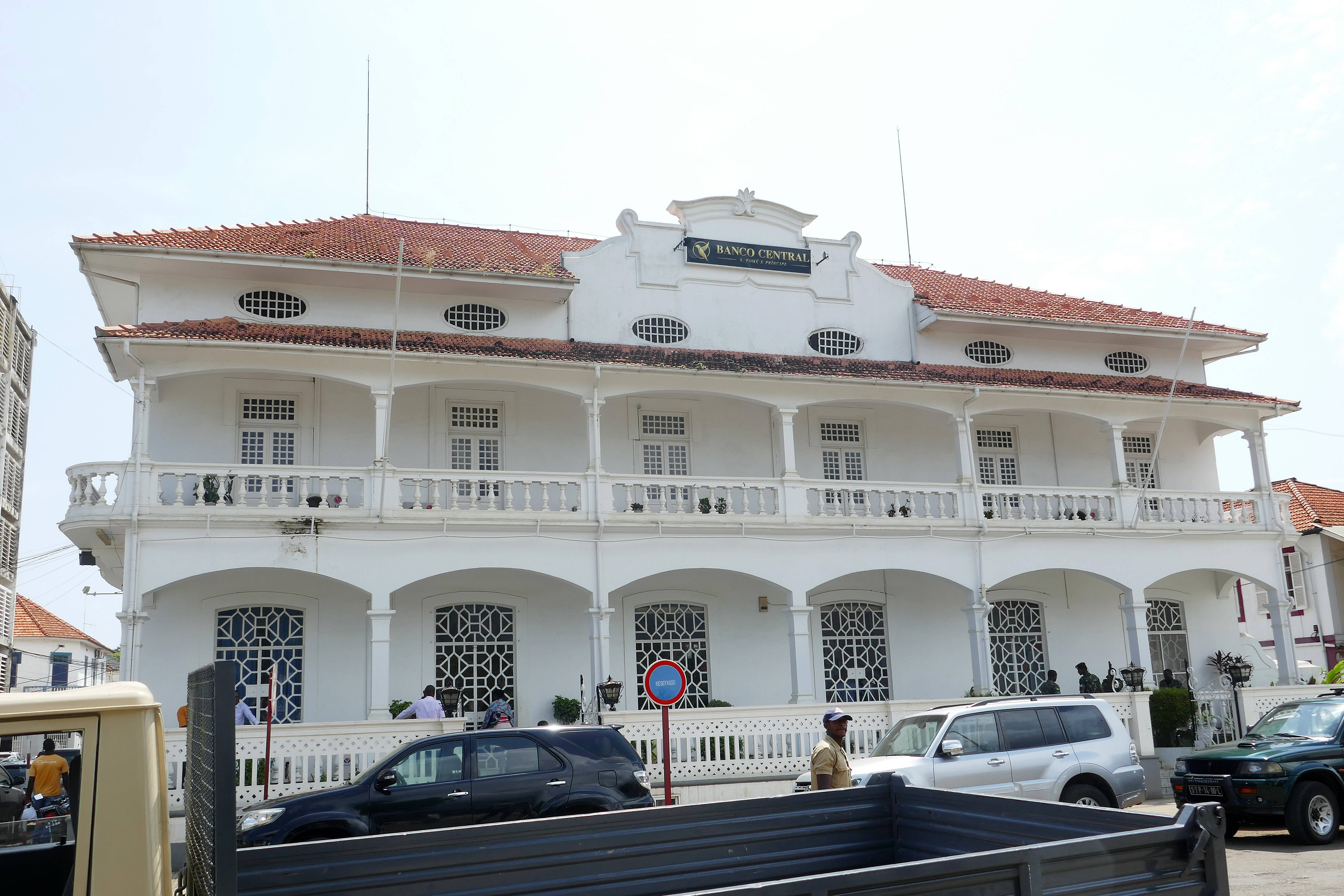 Building 桌布 壁紙 — 一座宏偉的白色殖民風格建築，擁有紅色瓦片屋頂和華麗的陽台，在明亮的日光下矗立，周圍停滿了汽車和行人。
