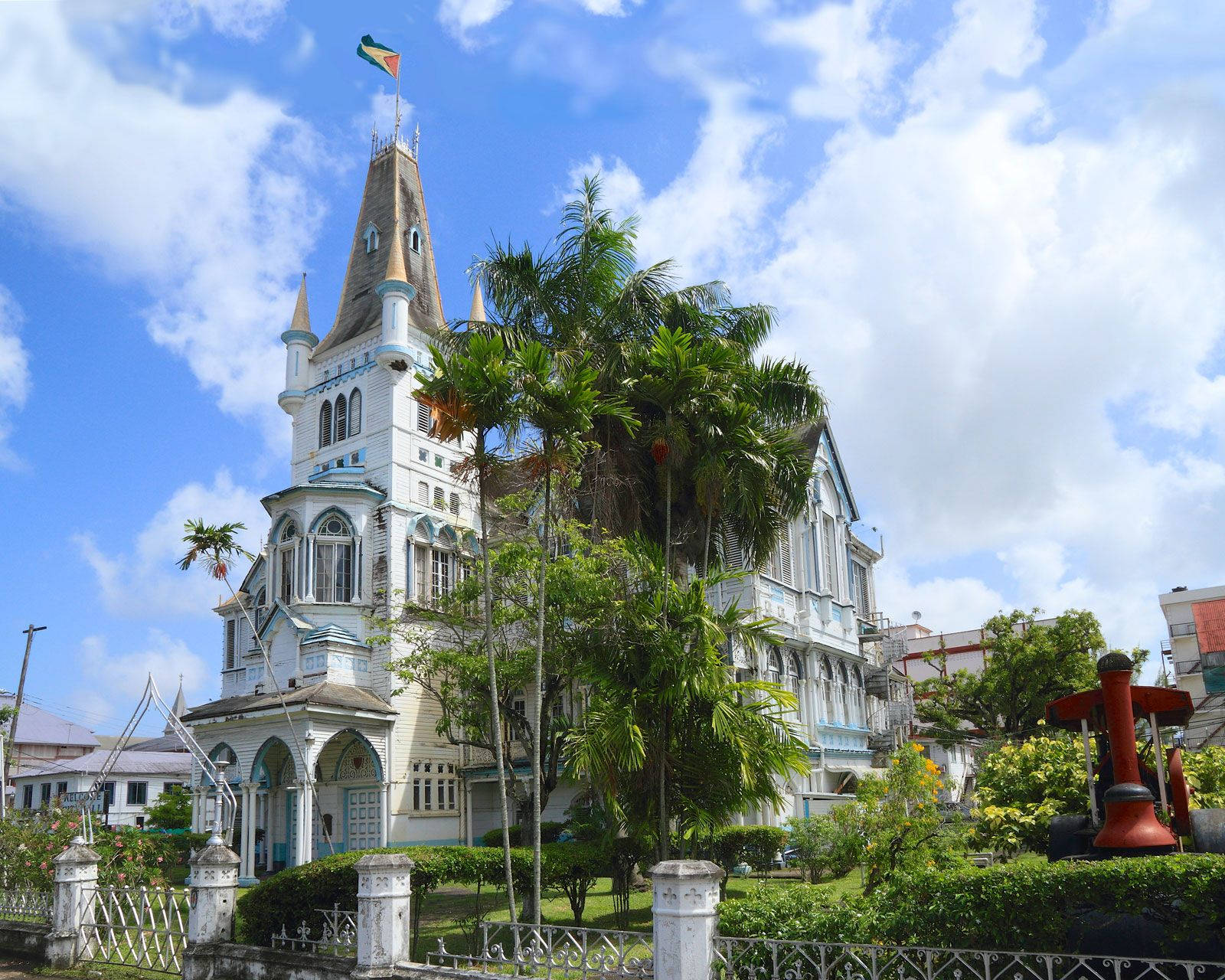 Guyana 桌布 壁紙 — 一座宏偉的白色殖民風格建築，高聳的尖頂和旗幟在藍天白雲下飄揚。