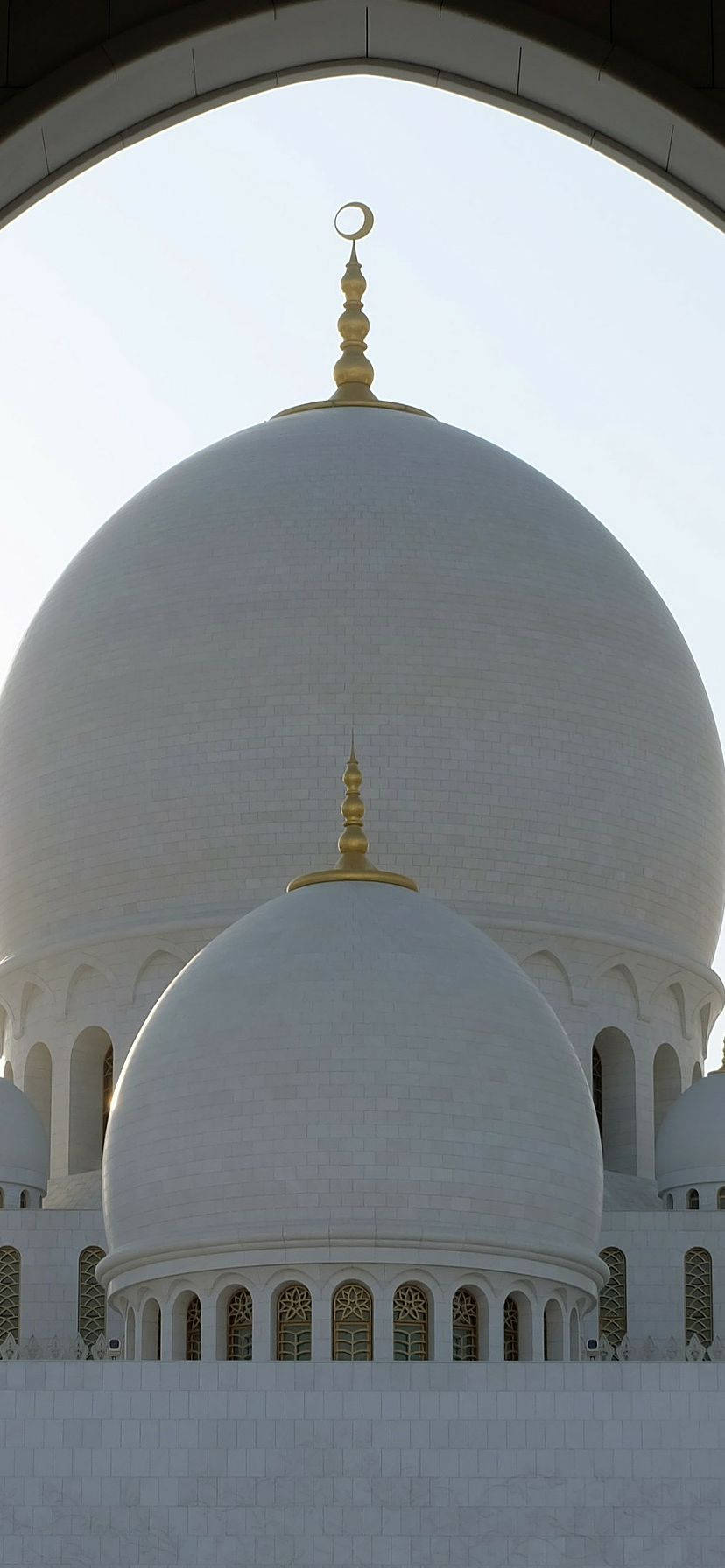 Best Islamic 桌布 壁紙 — 一座宏偉的白色清真寺圓頂，由帶有金色尖頂的拱門框住，在明亮的日光下閃耀。