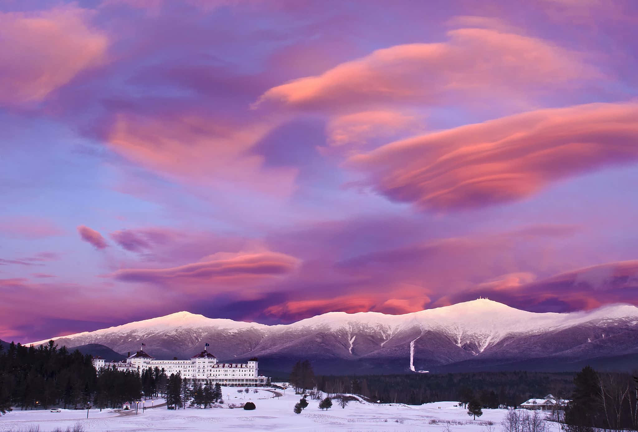Winter Landscape 桌布 壁紙 — 一座宏偉的白色酒店坐落在白雪皚皚的冬季景觀中，上方是戲劇性的粉紅色和紫色日落天空。