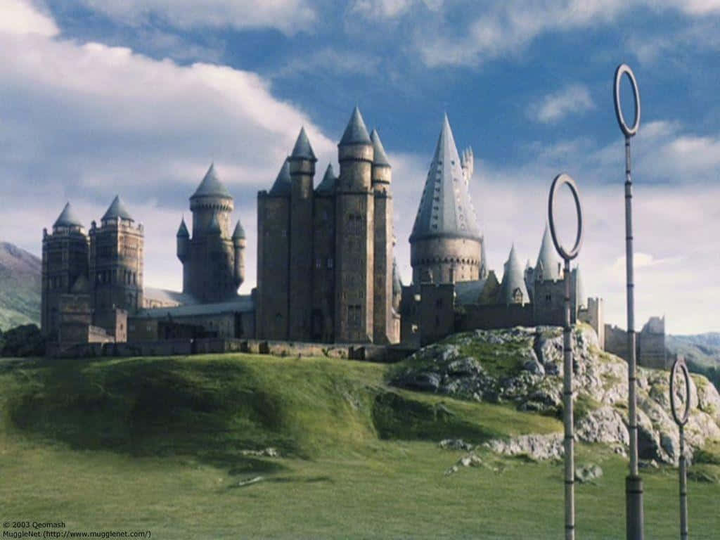 Hogwarts Castle 桌布 壁紙 — 一座宏偉的石城堡，帶有塔樓和尖塔，坐落於長滿青草的山丘上，藍天白雲之下。