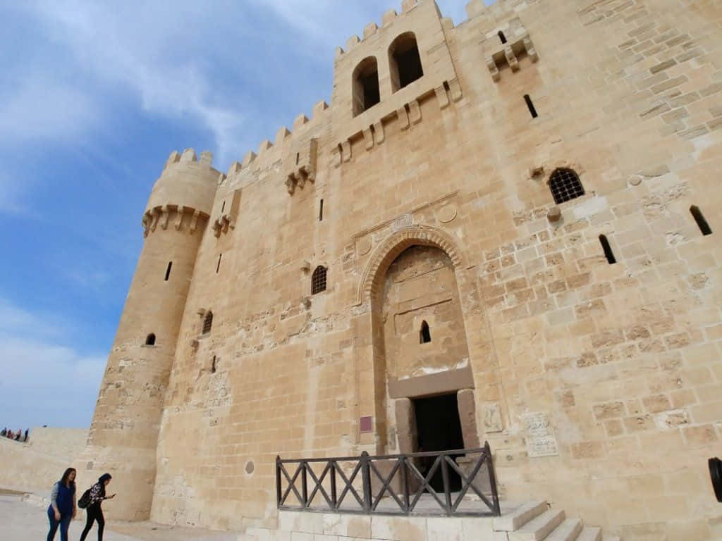 The Citadel 桌布 壁紙 — 一座宏偉的石城堡，擁有城垛塔樓和拱形入口，在明亮的藍天和薄雲下。